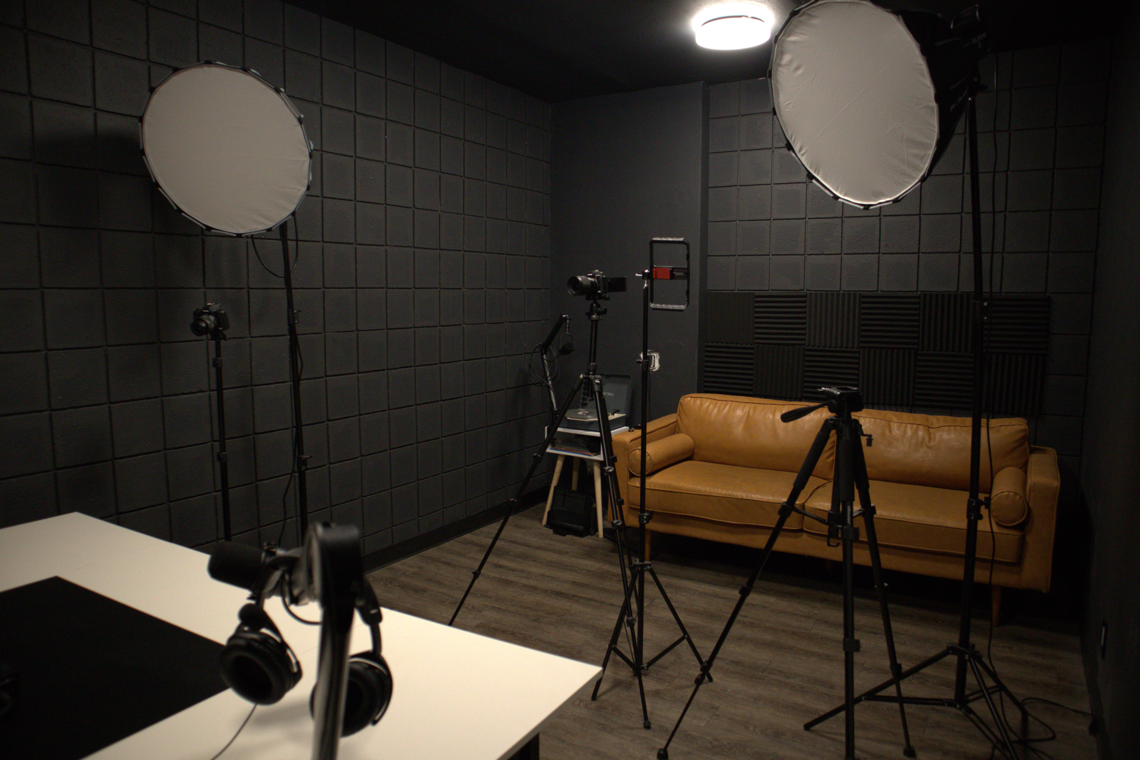 A photography studio with a tan couch, tripods, lighting equipment, and headphones arranged in a dark room.