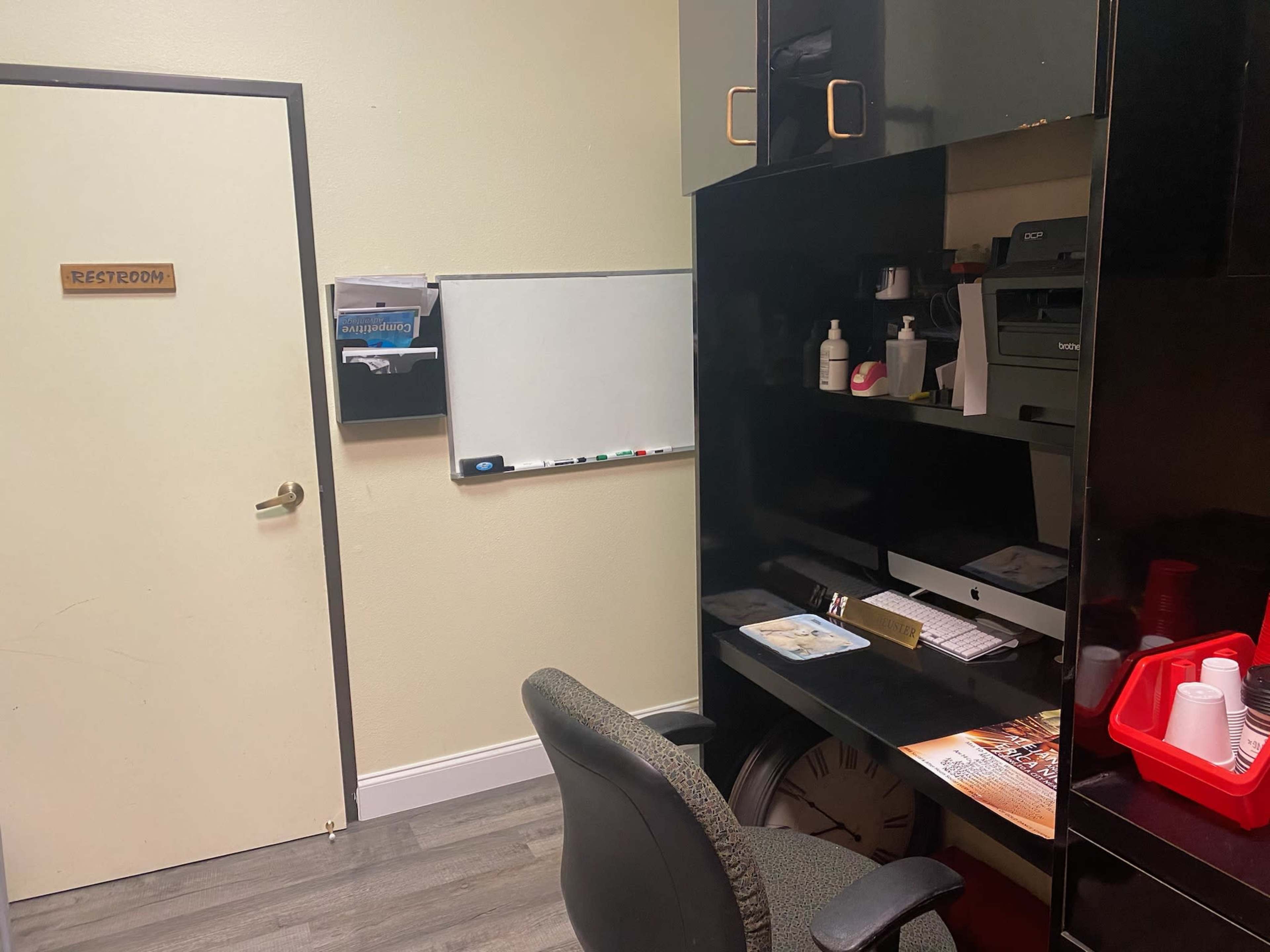The image shows an office space with a desk, a chair, a wall-mounted whiteboard, and a door labeled "Restroom."