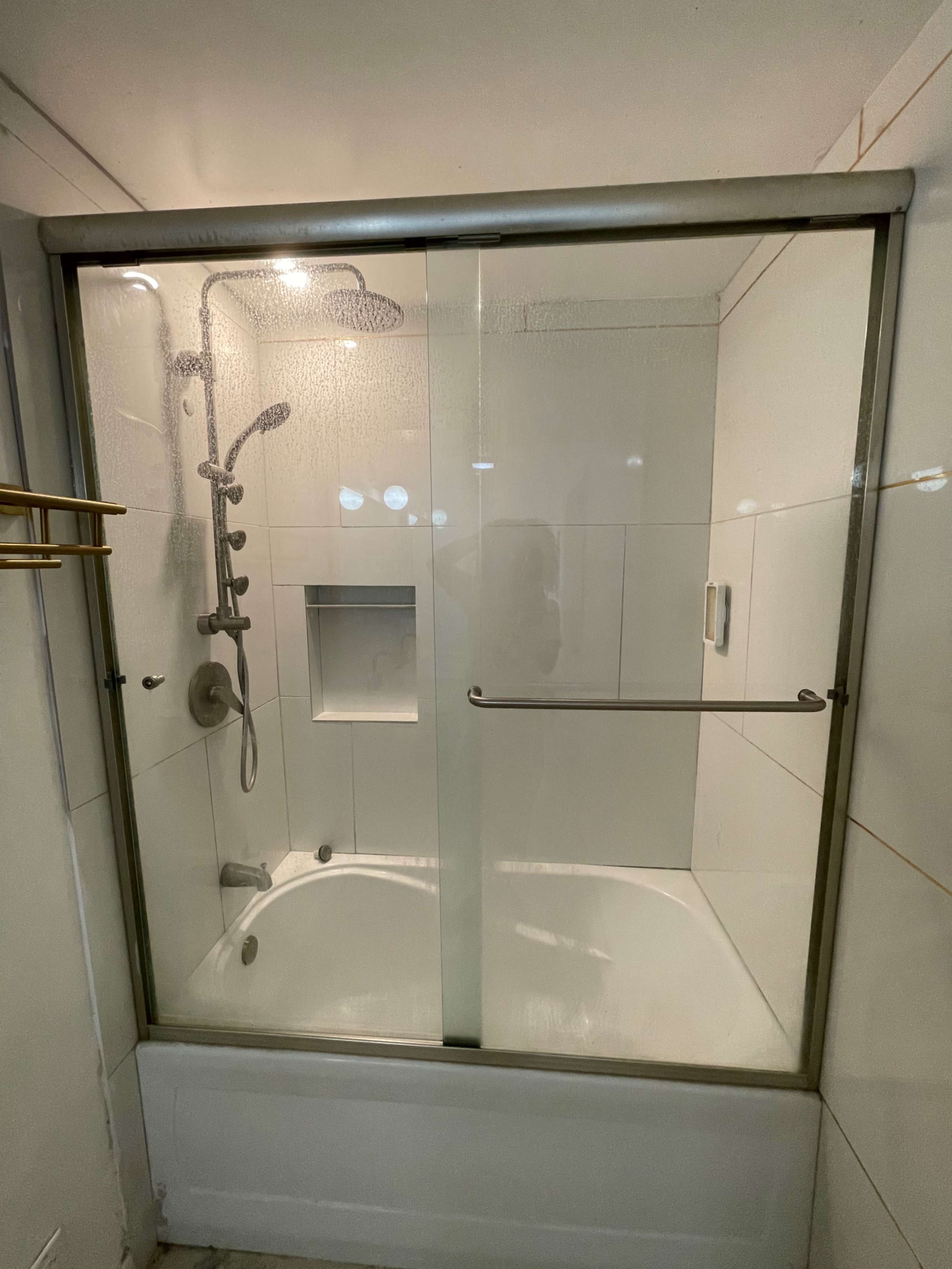 A glass-enclosed shower with a sliding door, featuring a showerhead and a built-in nook for toiletries.