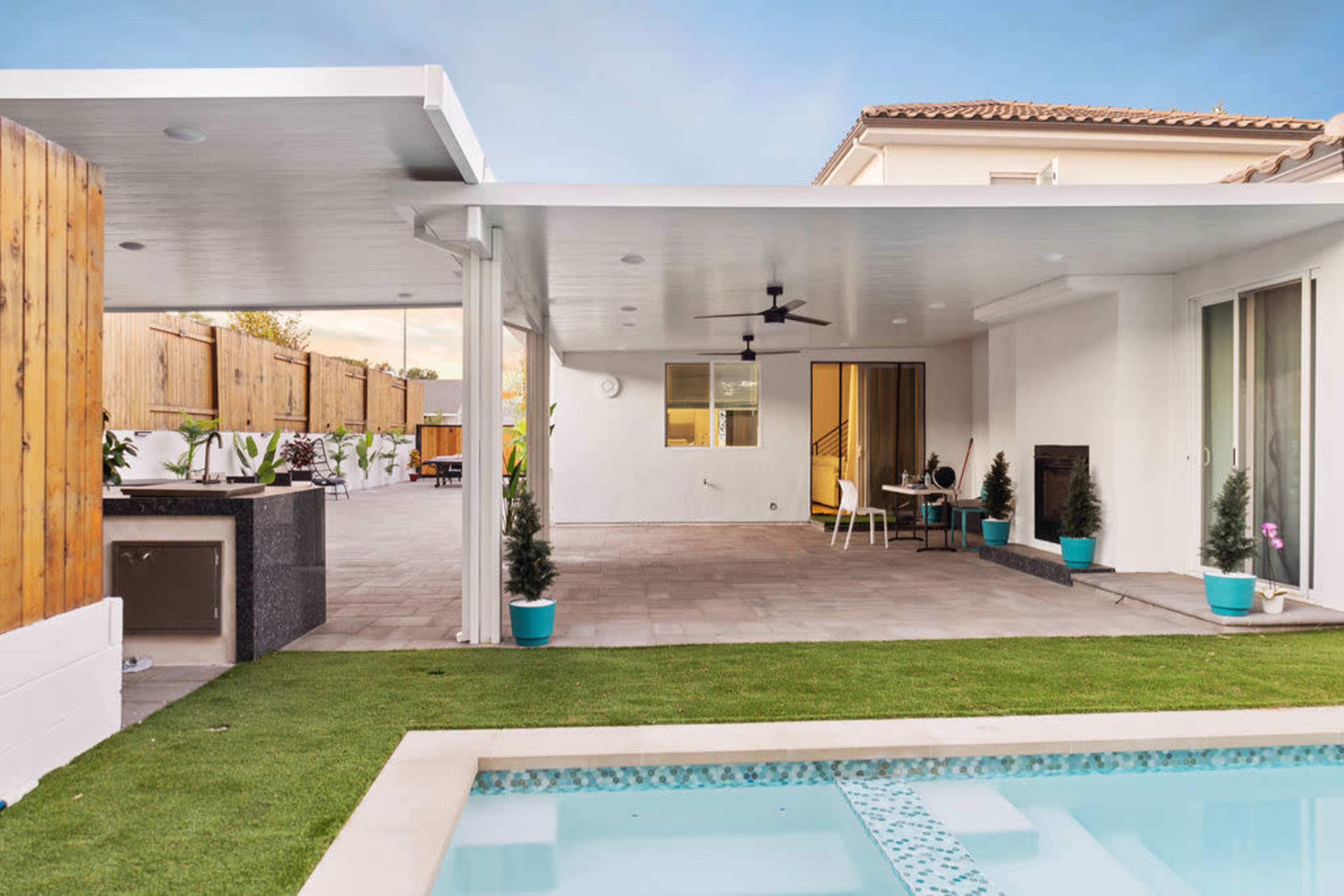 A modern outdoor area with a covered patio, a swimming pool, and neatly arranged greenery.