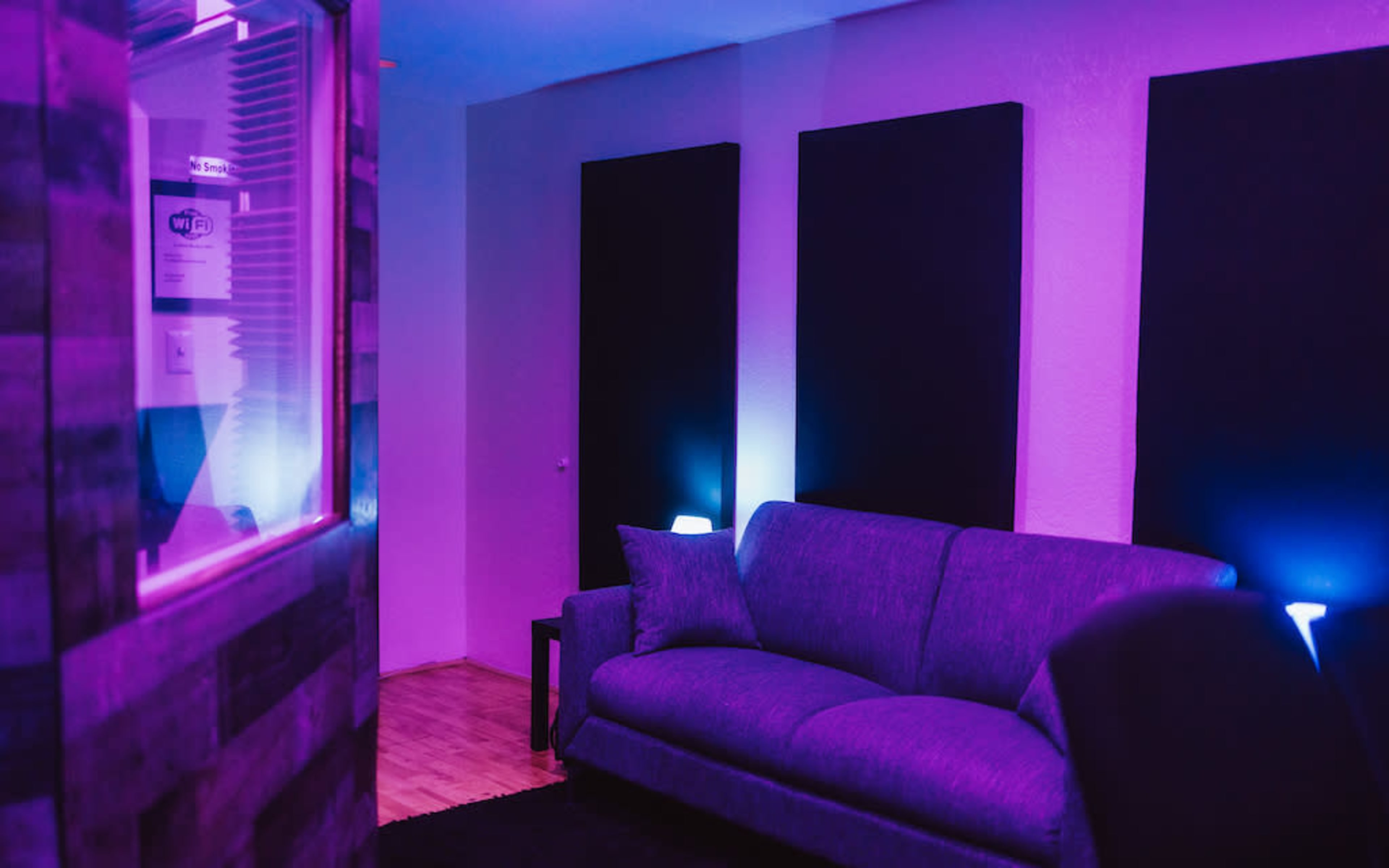 A modern room with purple lighting, featuring a gray sofa and black soundproofing panels on the walls.