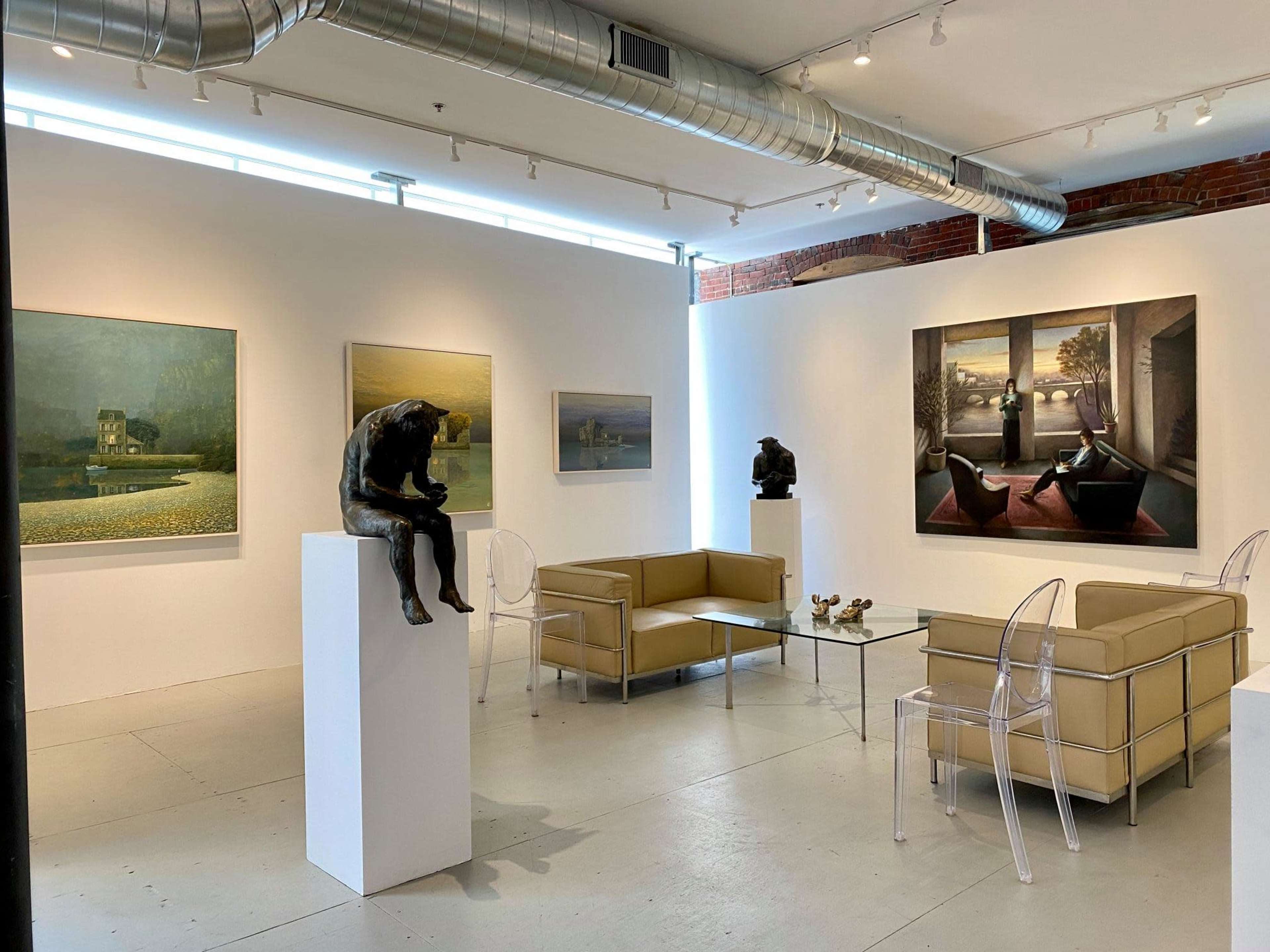A contemporary art gallery featuring several paintings on the walls and a sculpture seated on a pedestal in the center, with modern furniture arranged in a seating area.