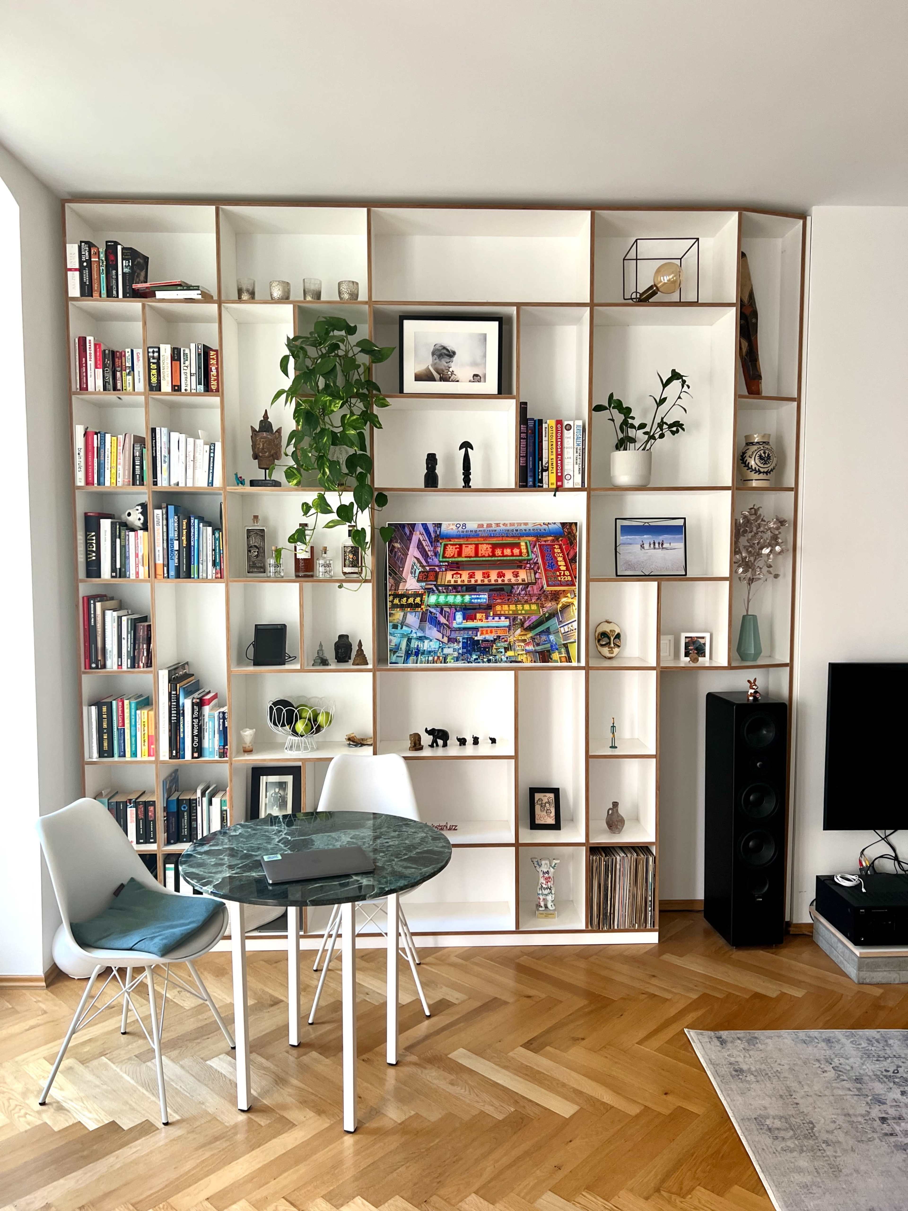 A modern living space features a built-in bookshelf filled with books and decorative items, next to a small round dining table with two chairs.