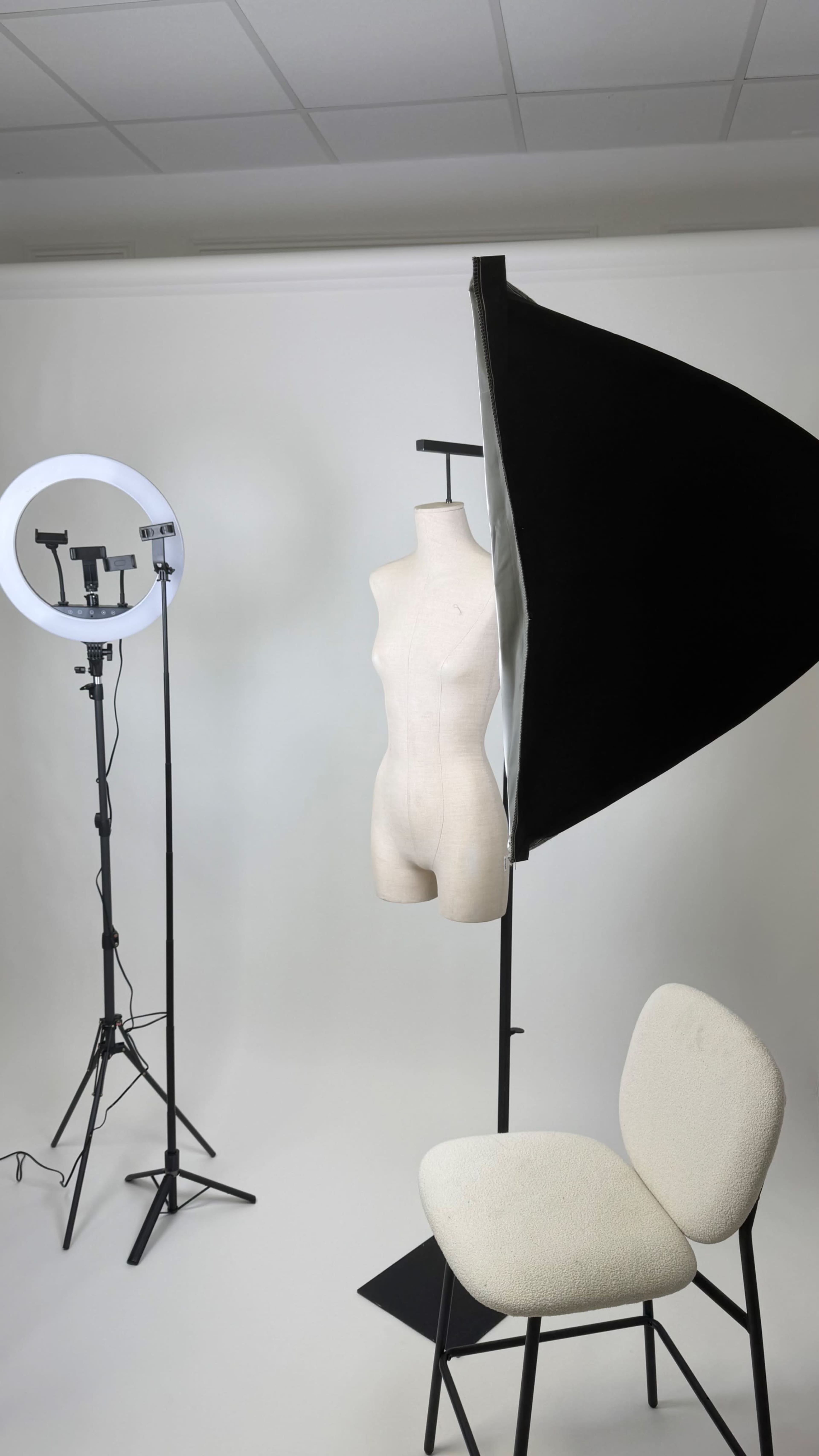 The image shows a photography studio setup featuring a mannequin on a stand, a circular light, and a softbox light near a chair.
