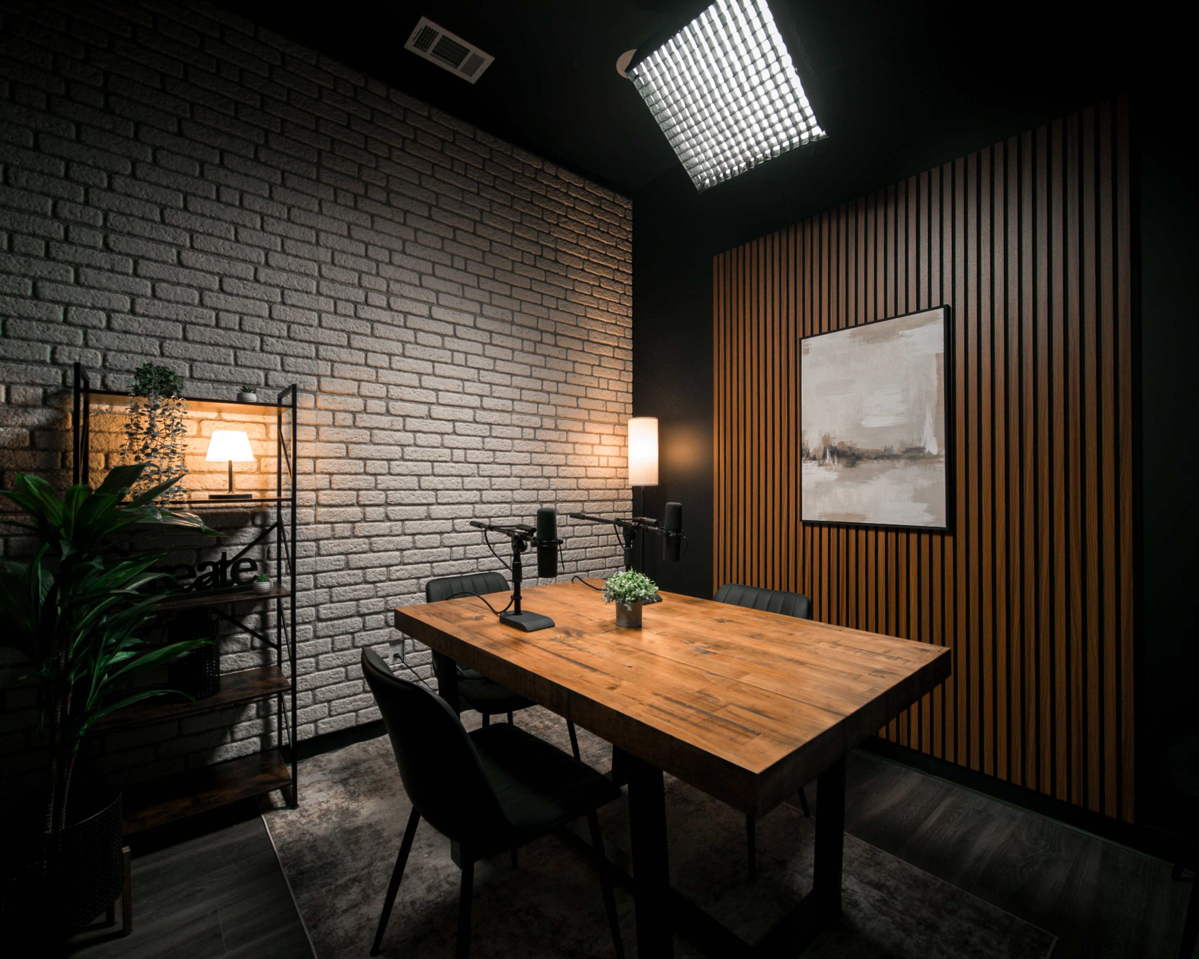 The image shows a modern conference room with a wooden table, black chairs, and a microphone setup against a backdrop of textured brick and wooden walls.