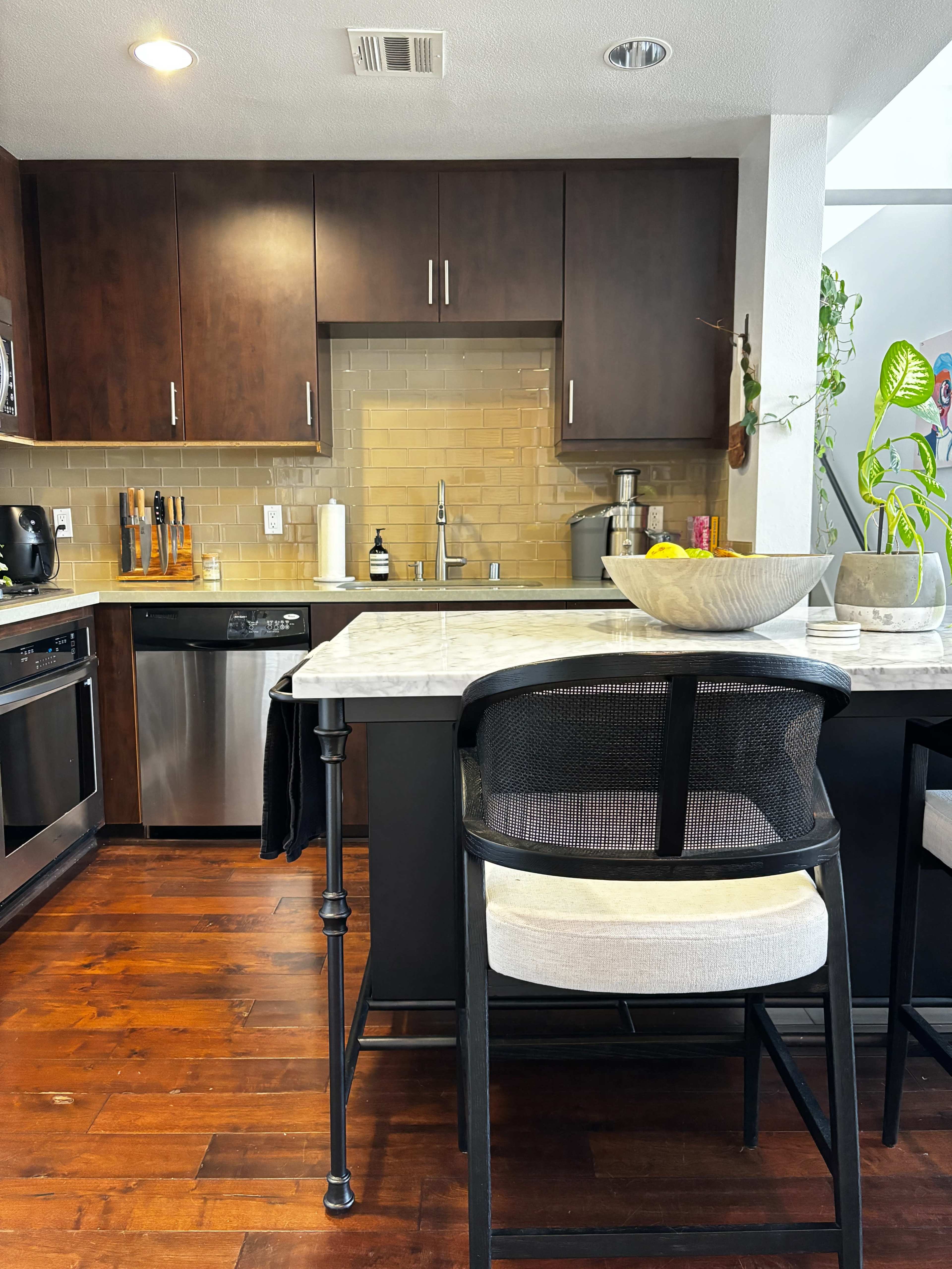A modern kitchen features dark cabinetry, a marble countertop island with a bowl of fruit, and stainless steel appliances.