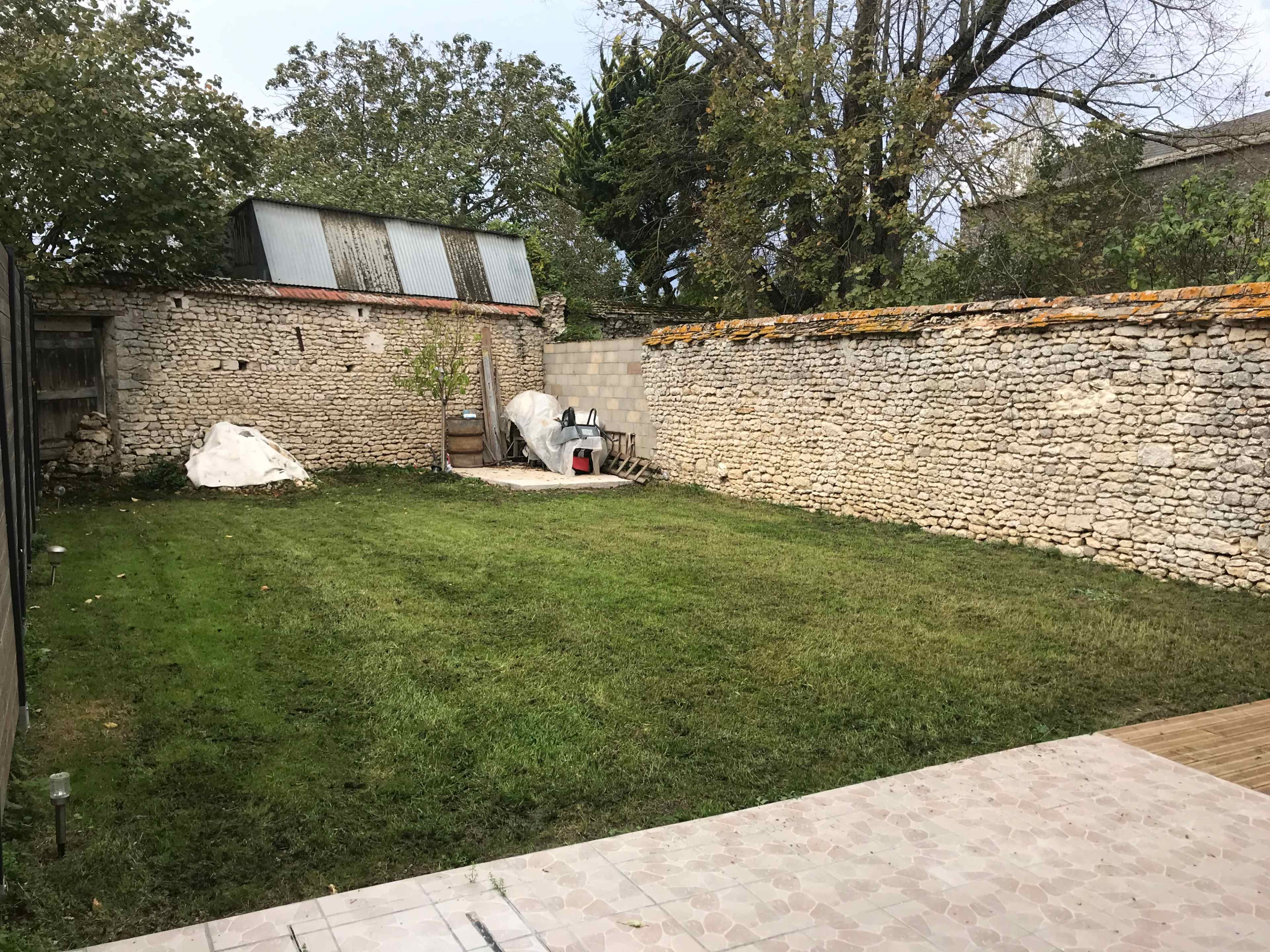 A spacious garden enclosed by stone walls, featuring a grassy area and a decorative sculpture resembling a wolf.