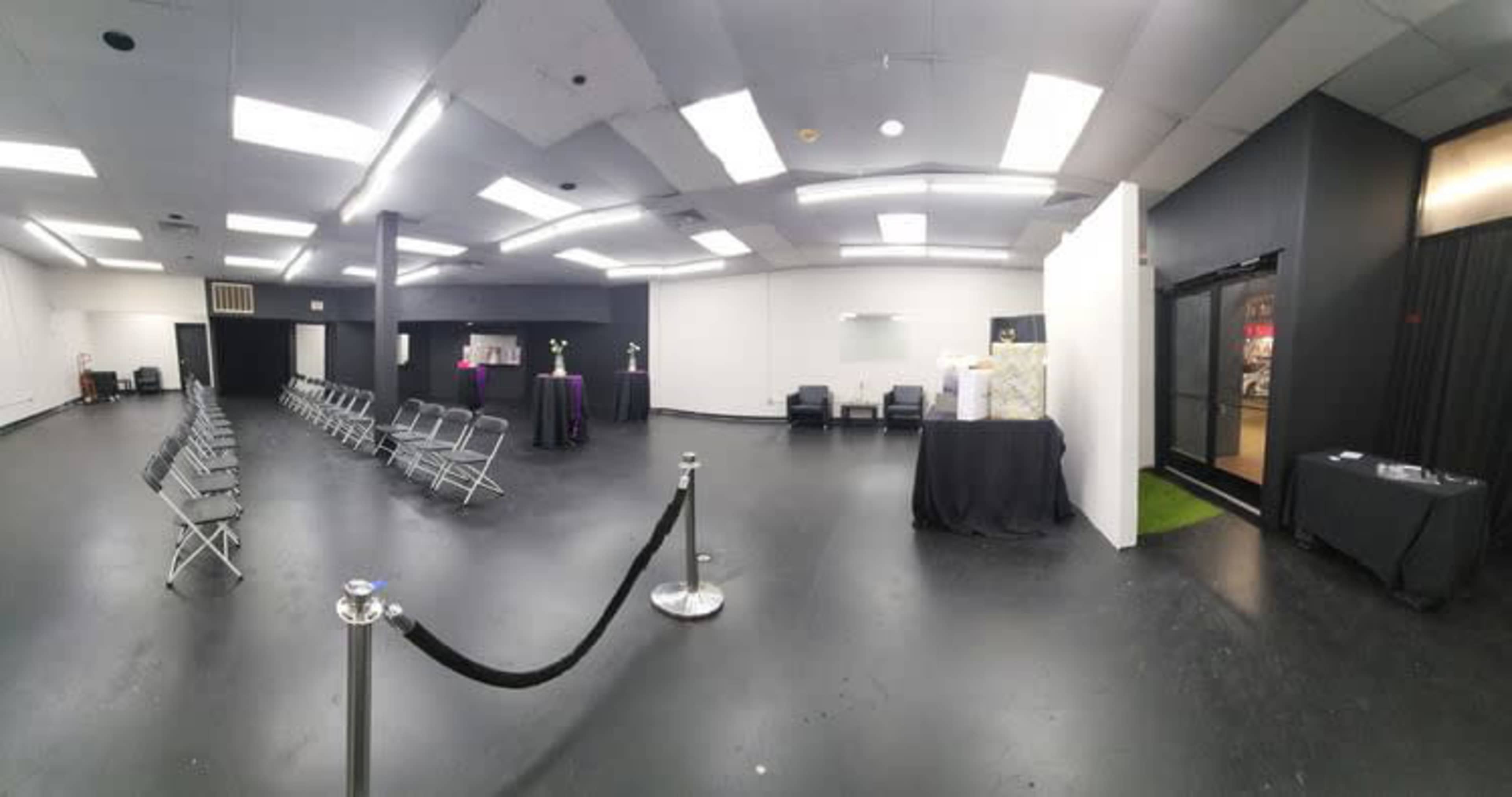 A spacious, empty room with rows of metal chairs facing a central area and several tables along the walls.