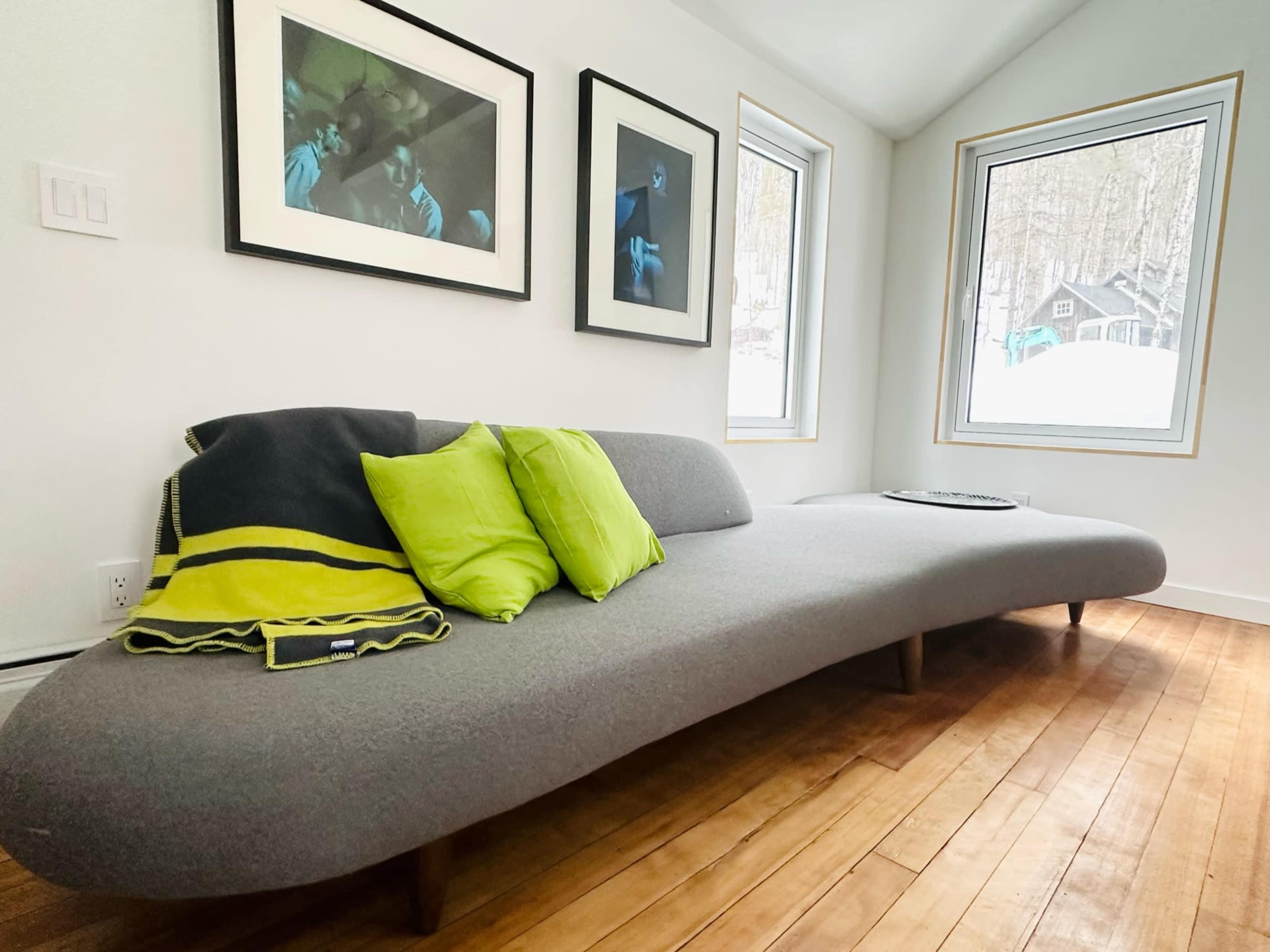 A modern, curved gray sofa with green accent pillows in a bright room featuring large windows and framed photographs on the walls.