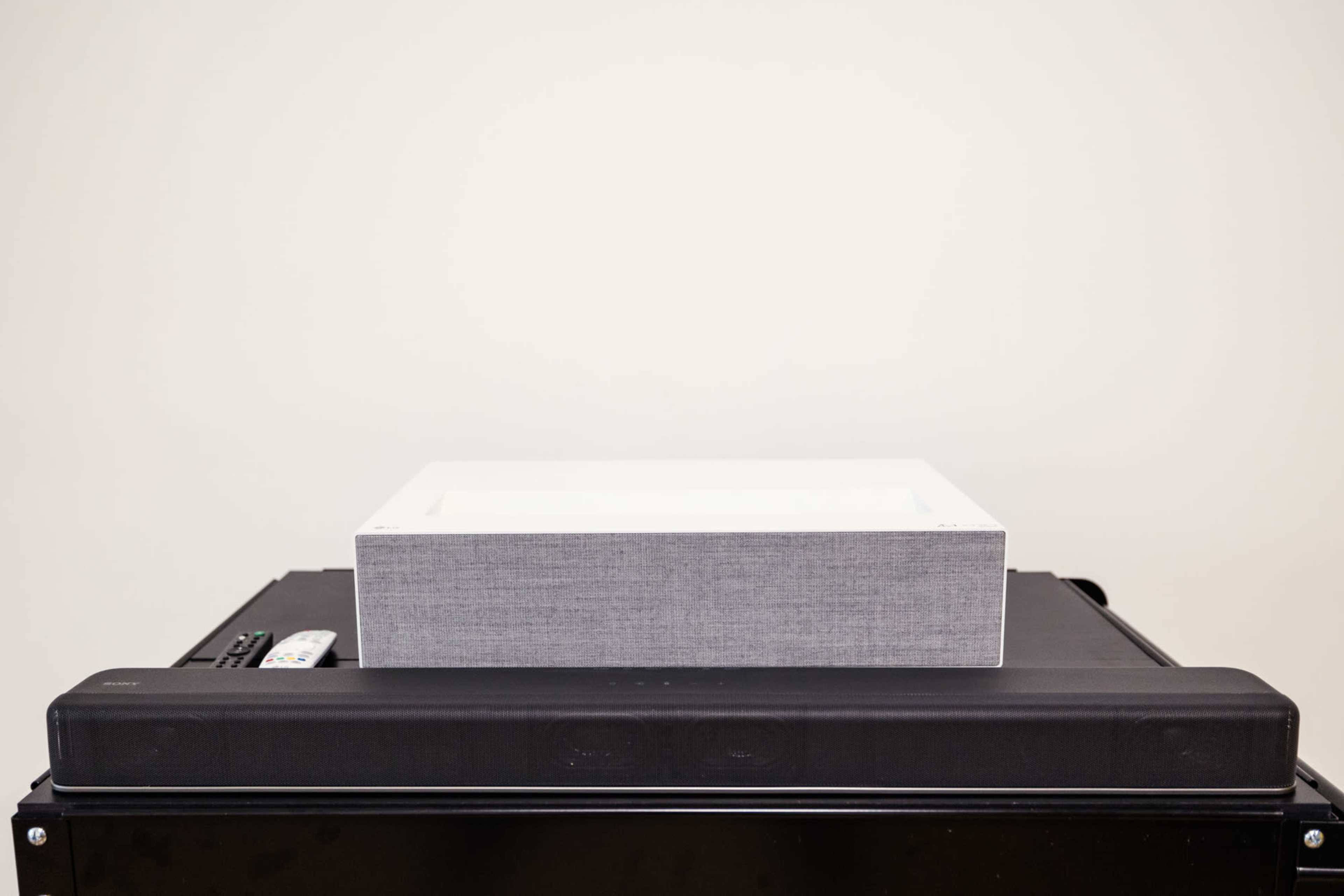 A gray rectangular box sits atop a black electronic device in front of a plain white wall.