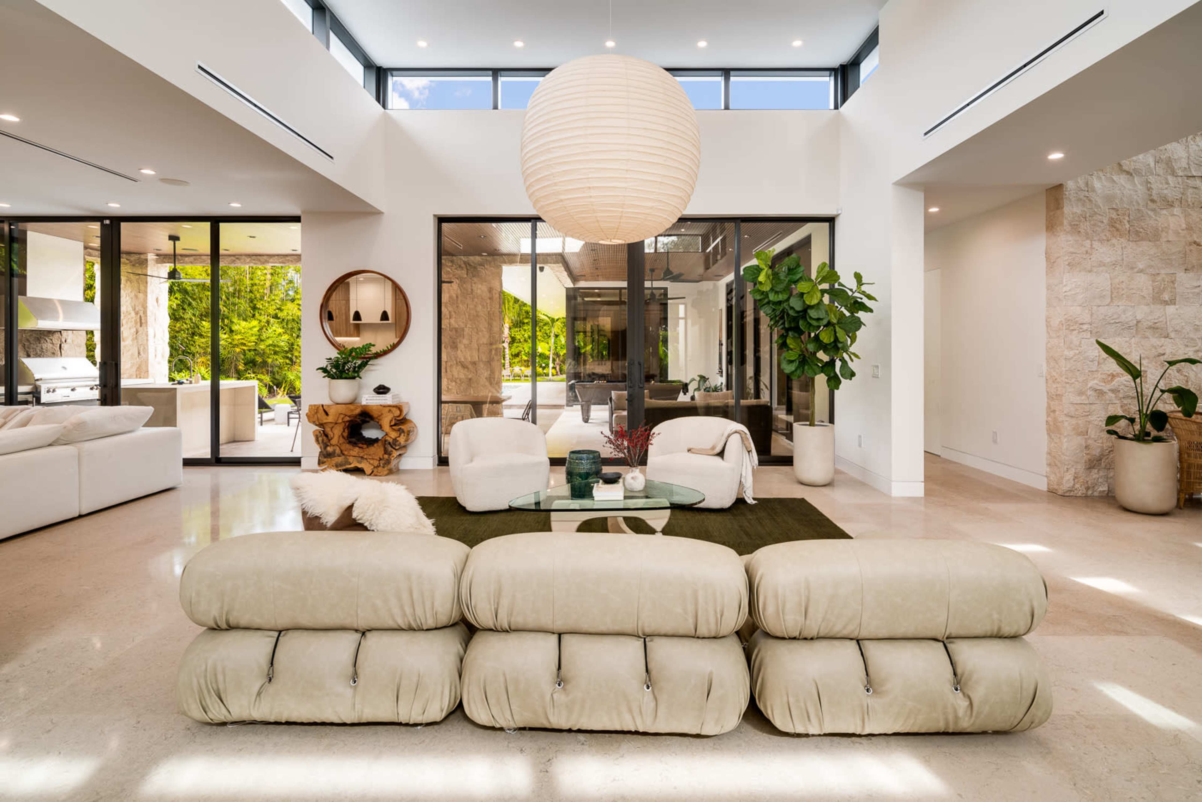 A modern living room with a light-colored sofa facing a round coffee table, large windows, and a paper lantern hanging from the ceiling.