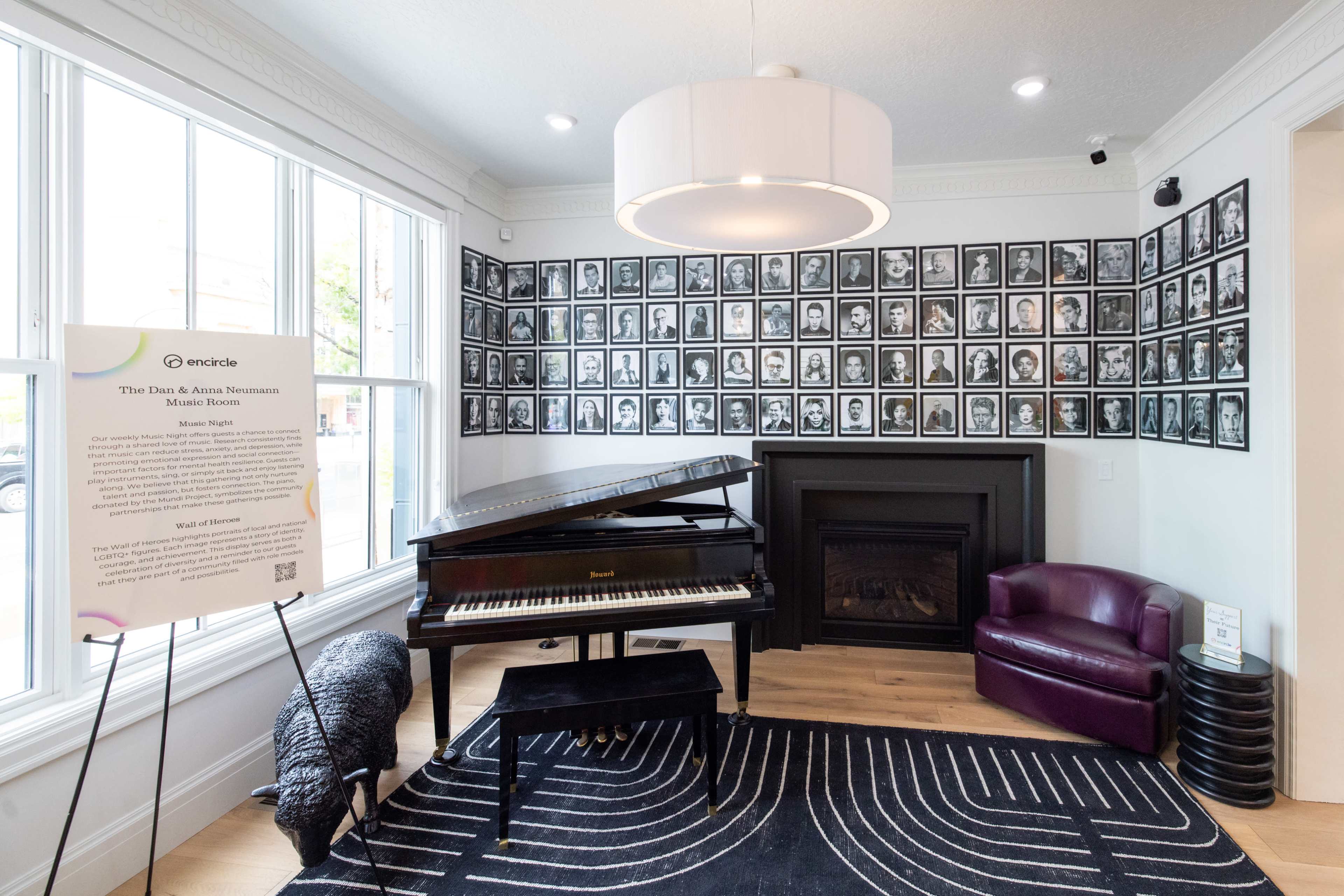 The image shows a room featuring a grand piano, a purple armchair, a modern light fixture, and a wall adorned with numerous black-and-white framed portraits.
