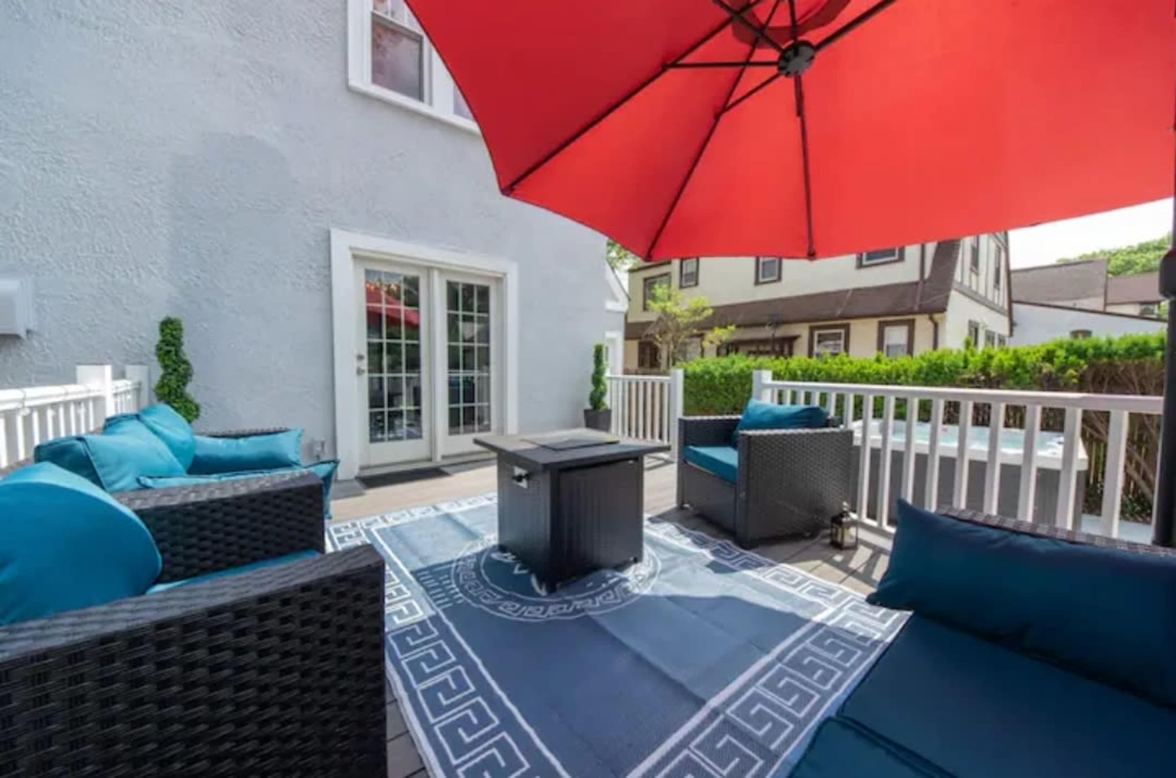 A patio area features wicker seating with blue cushions, a red umbrella, and a small table on a decorative rug.