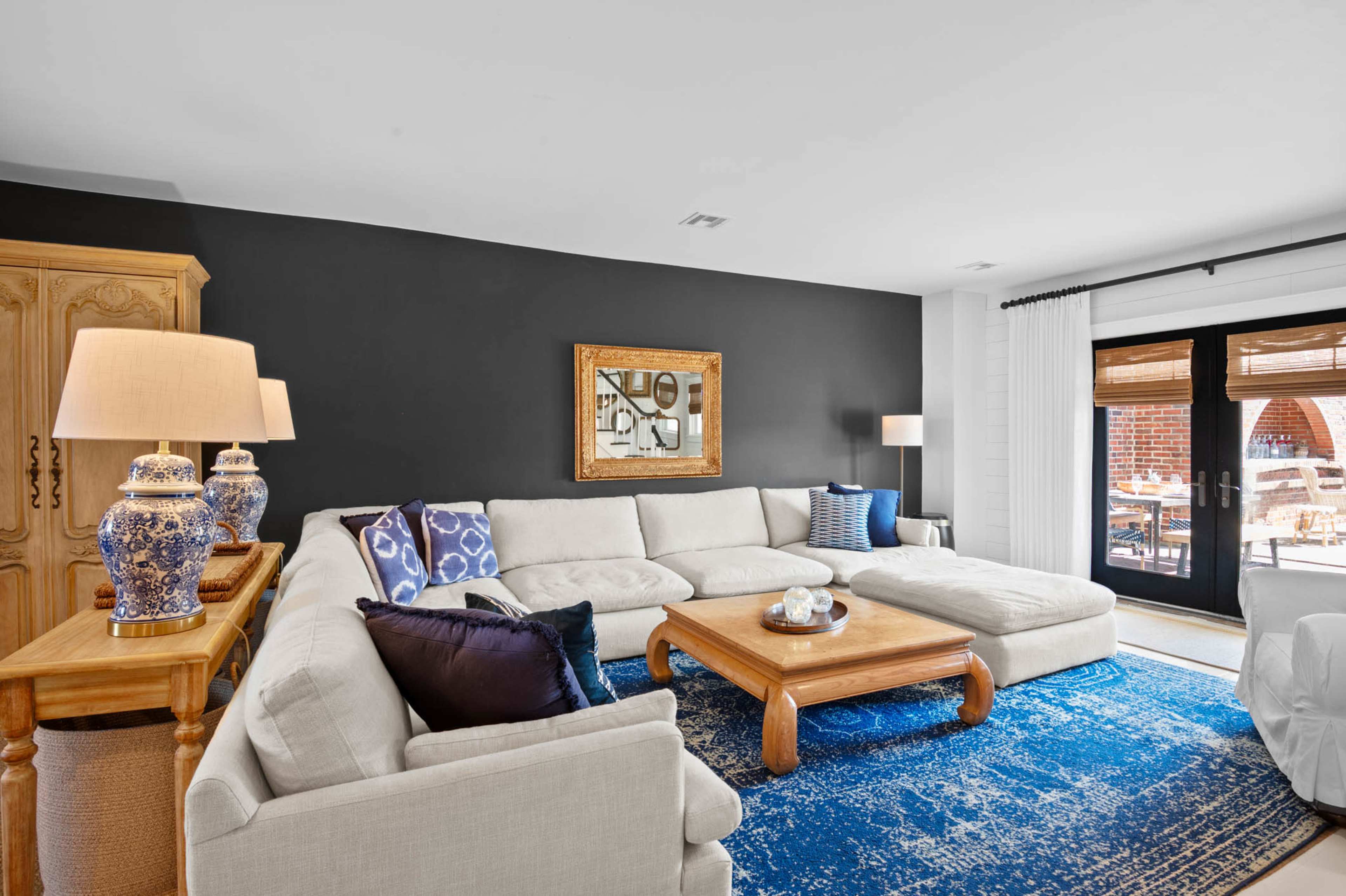 The living room features a large sectional sofa, a wooden coffee table, and decorative lamps, with dark walls and a blue area rug.
