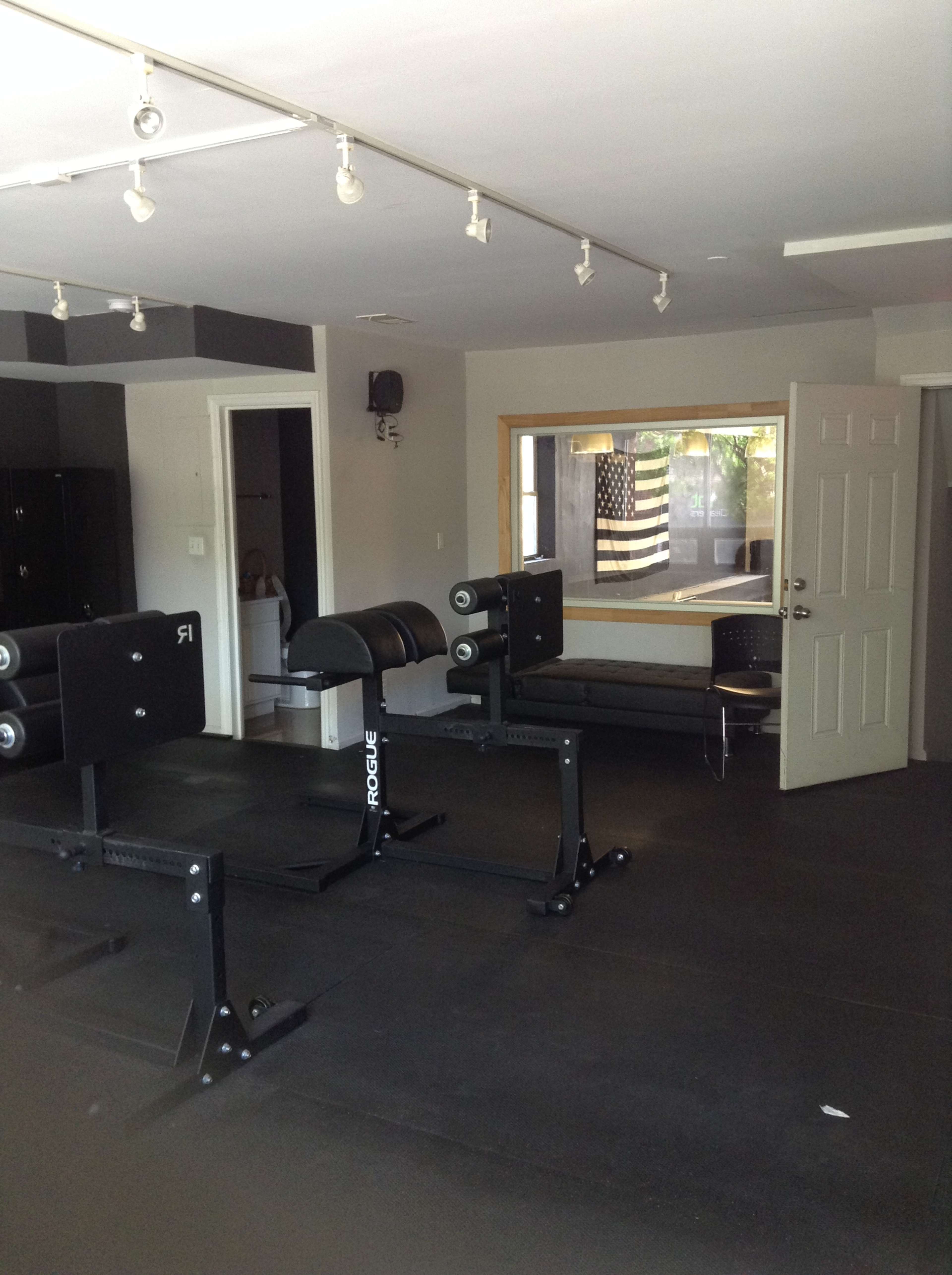 A gym interior with weightlifting equipment, a bench, and a visible American flag in a window.