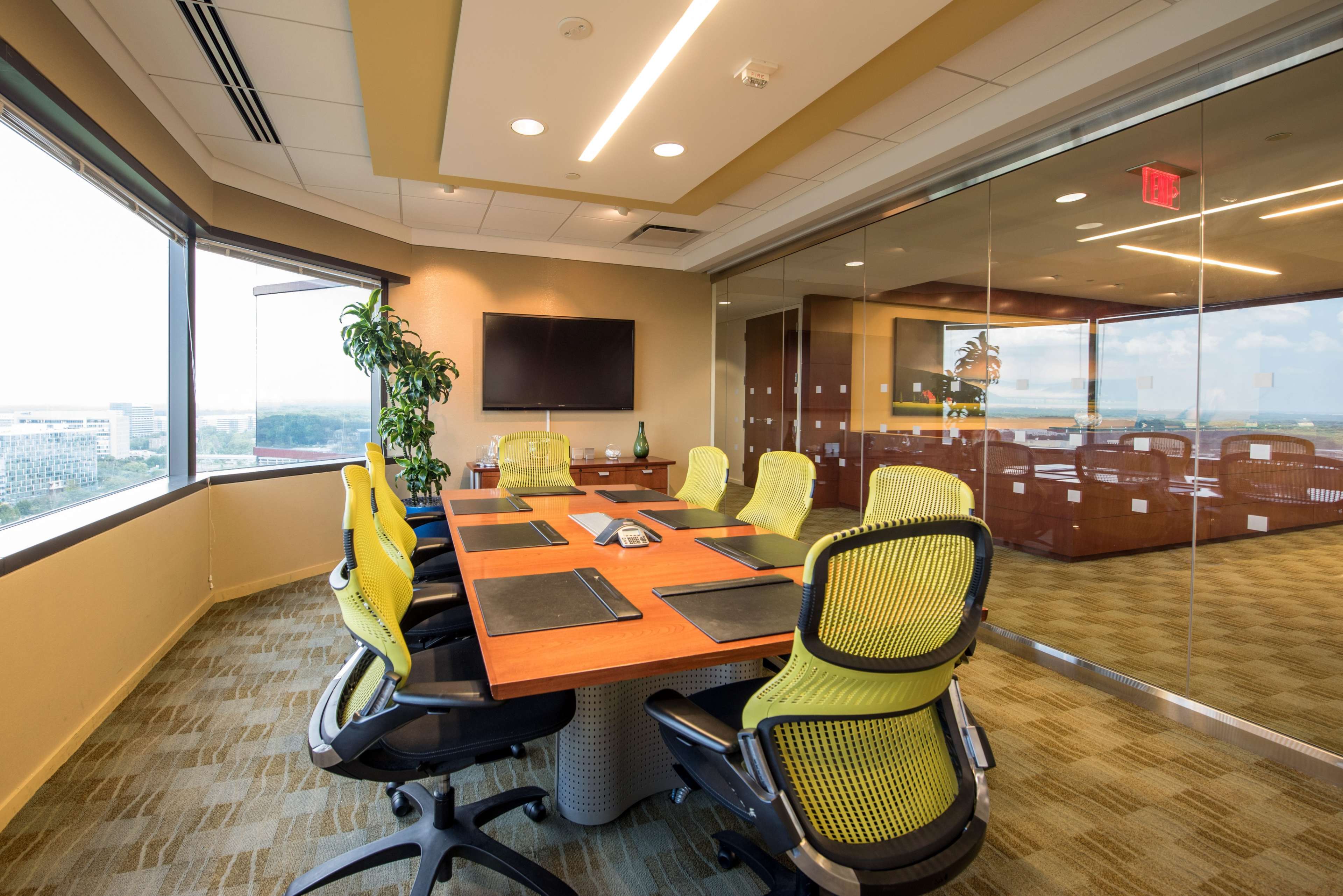 A modern conference room features a large table surrounded by ergonomic chairs, with a view of the city through floor-to-ceiling windows.