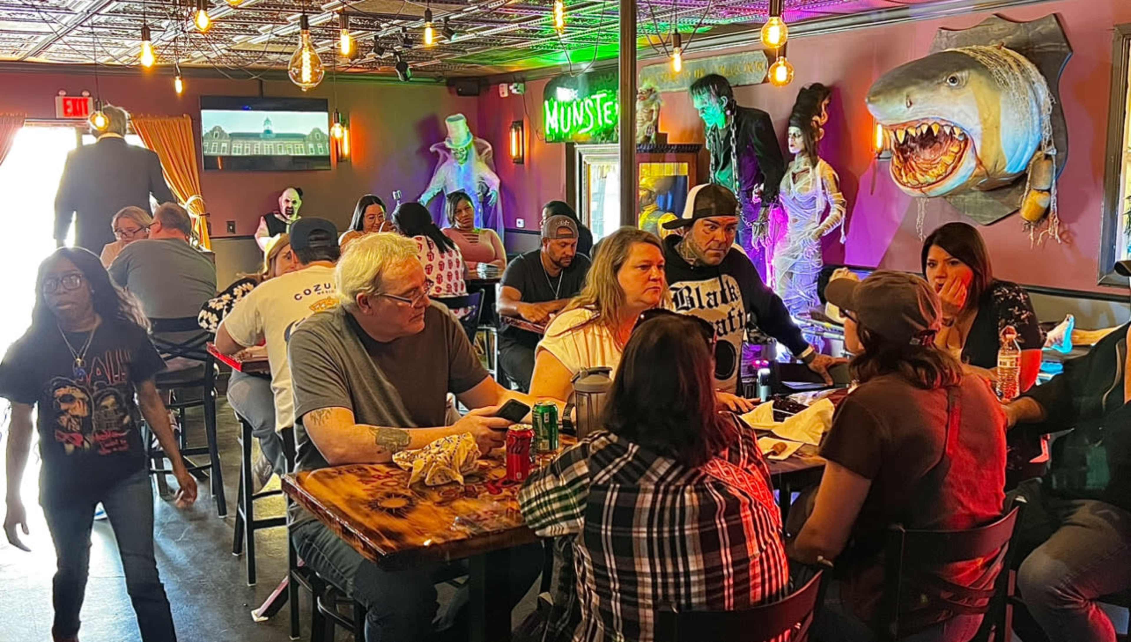 A busy restaurant scene features patrons enjoying food and drinks, with vibrant decor and themed decorations on the walls.