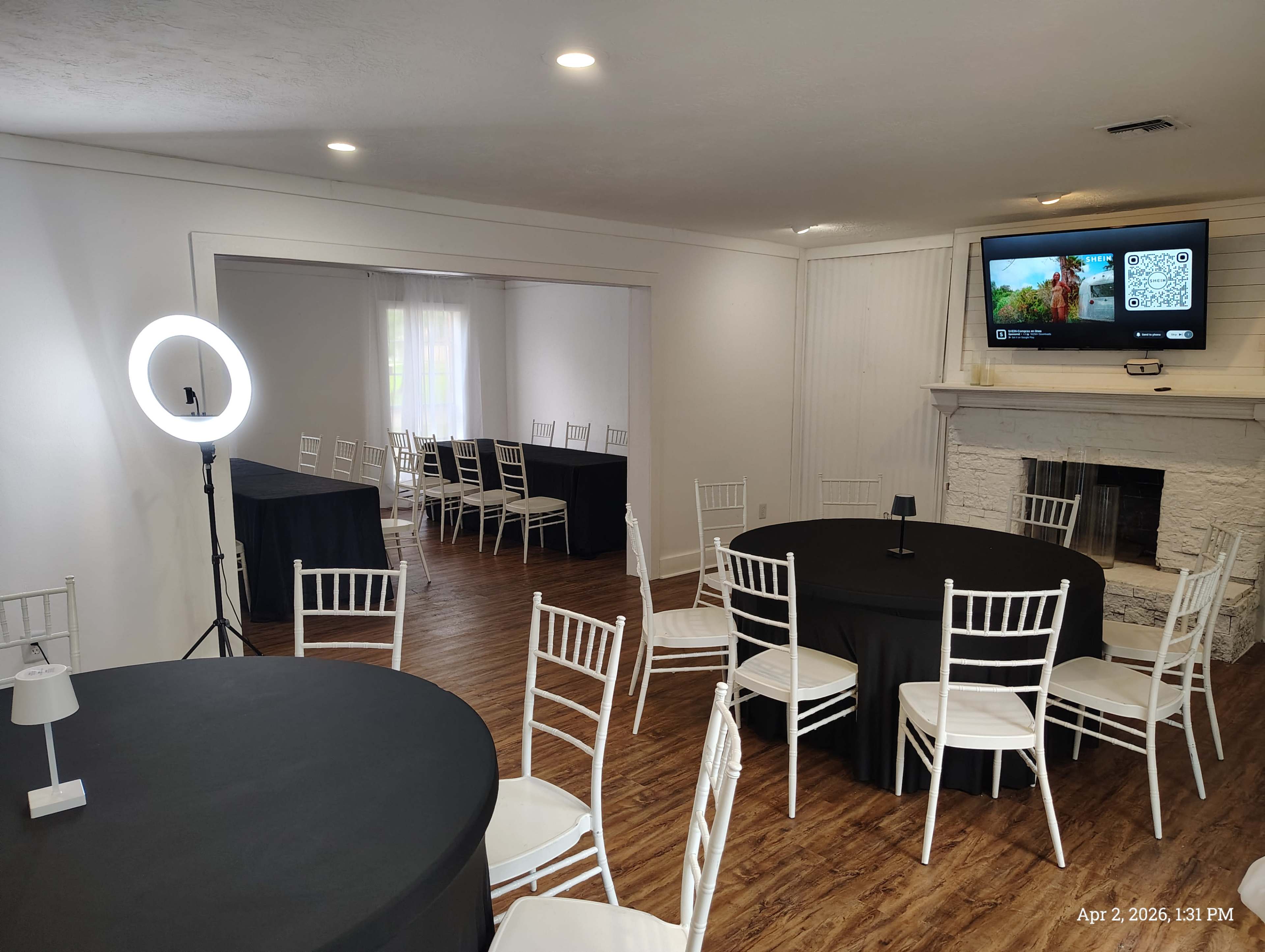 The image shows a spacious event room with several tables covered in black tablecloths, white chairs, and a wall-mounted screen displaying QR codes and a promotional image.