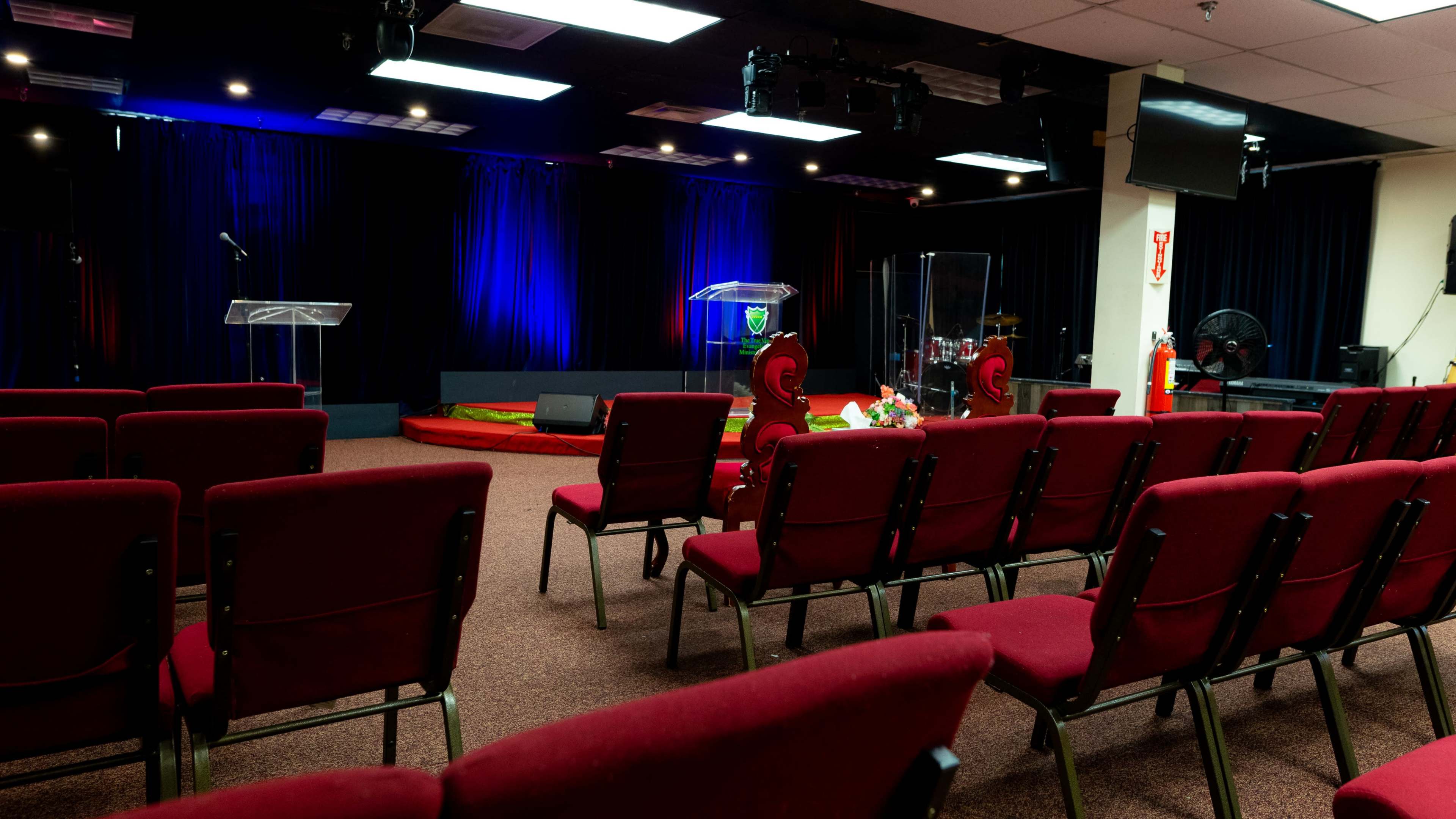 A church sanctuary with rows of red chairs facing a transparent podium and a drum set in the background.