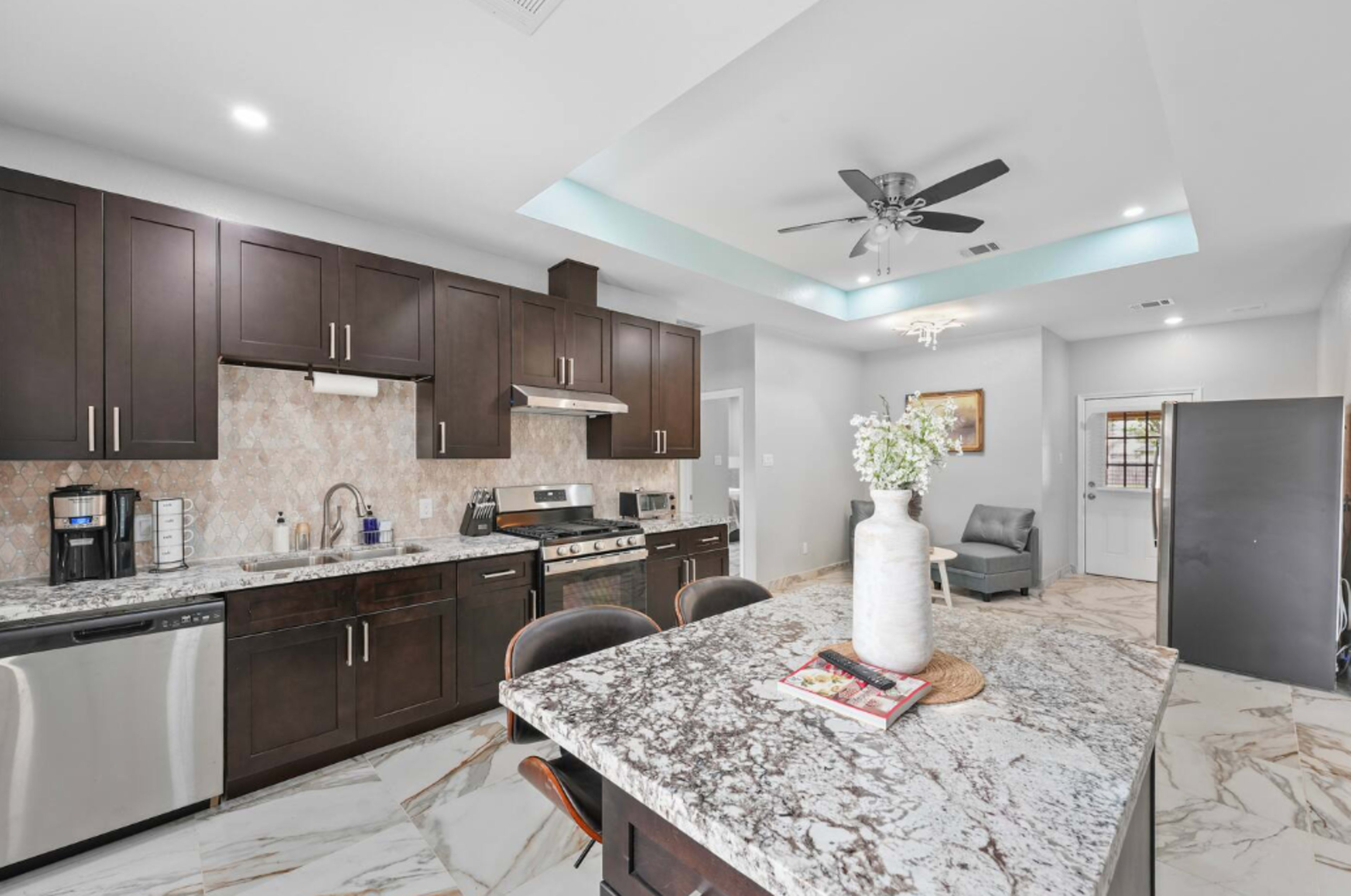 The image shows a modern kitchen with dark cabinetry, stainless steel appliances, and a large island featuring a marble countertop.