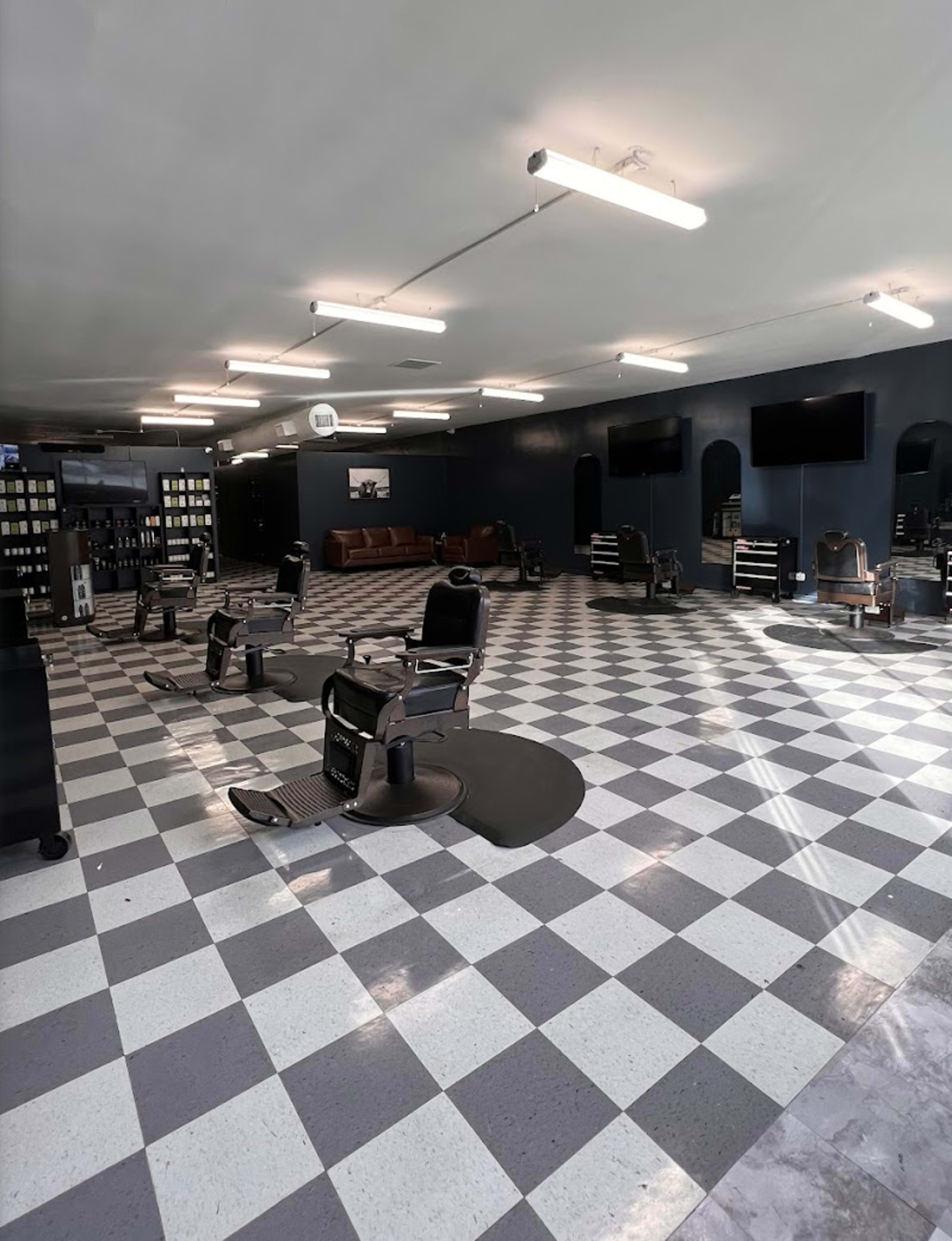 The image shows an empty barbershop with multiple styling chairs arranged in a checkerboard-patterned floor and dark blue walls.