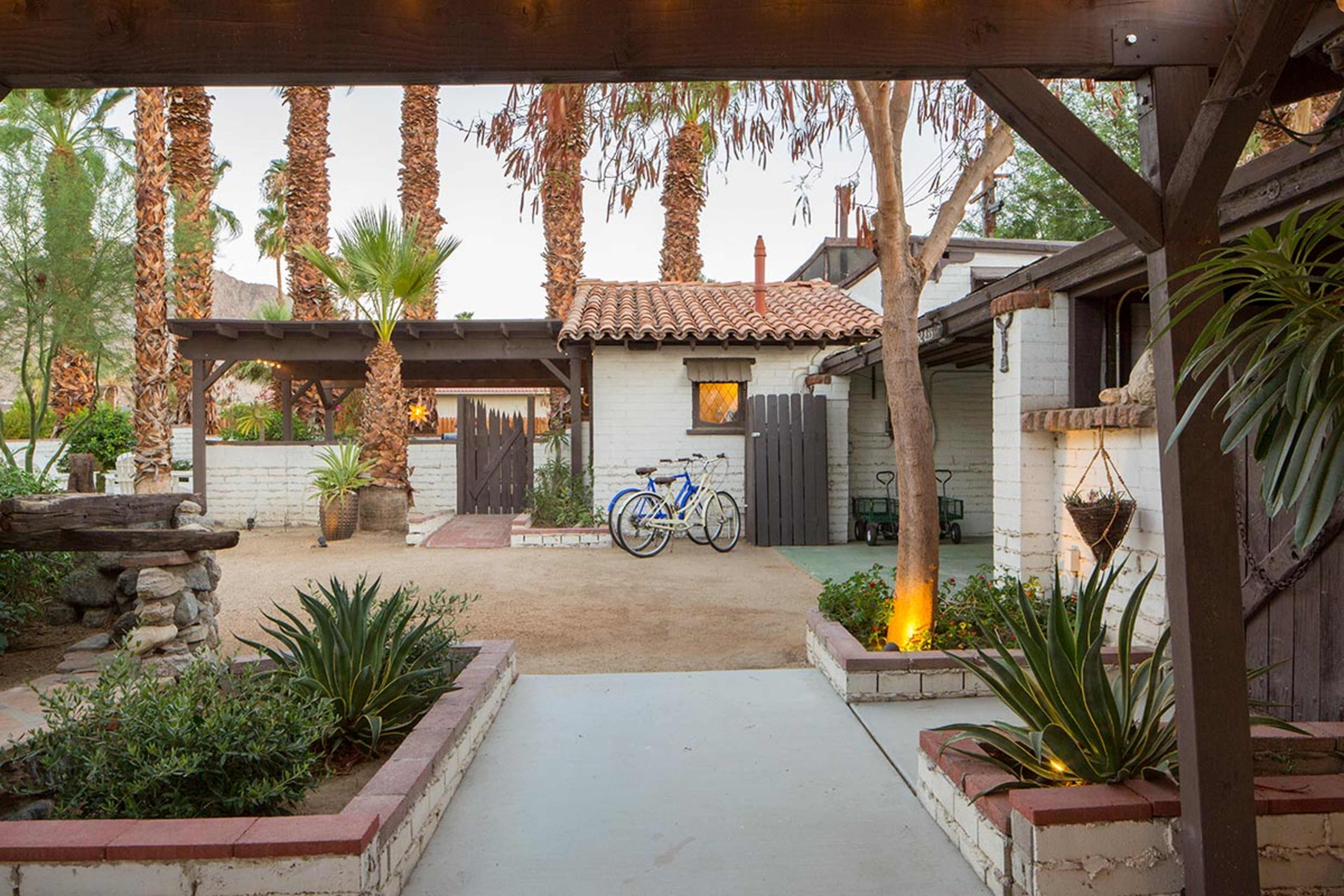 A peaceful courtyard with palm trees, a gravel path, and bicycles parked near a white brick building.