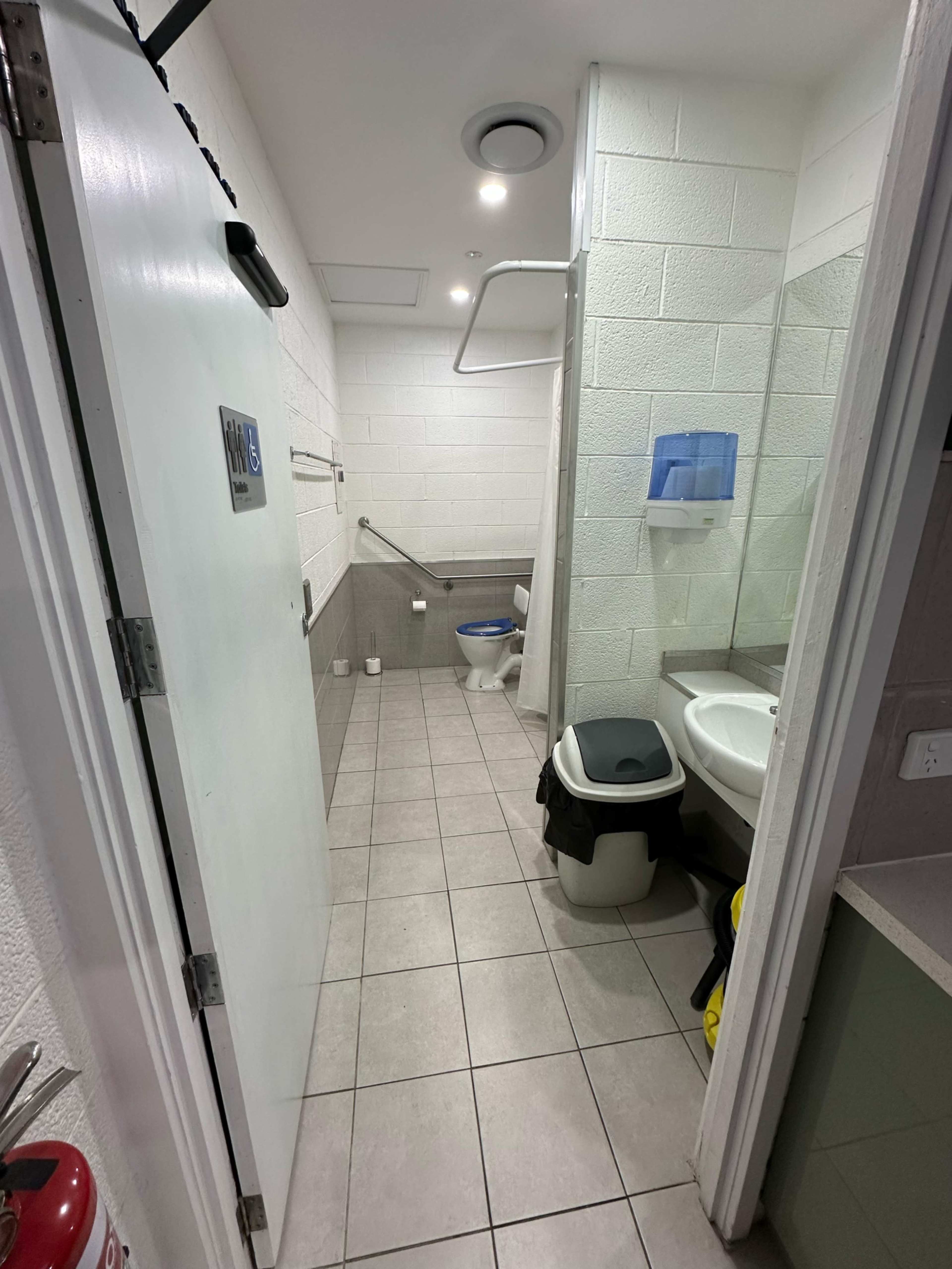 The image shows a restroom with a toilet, sink, a trash bin, and tiled walls and floor.