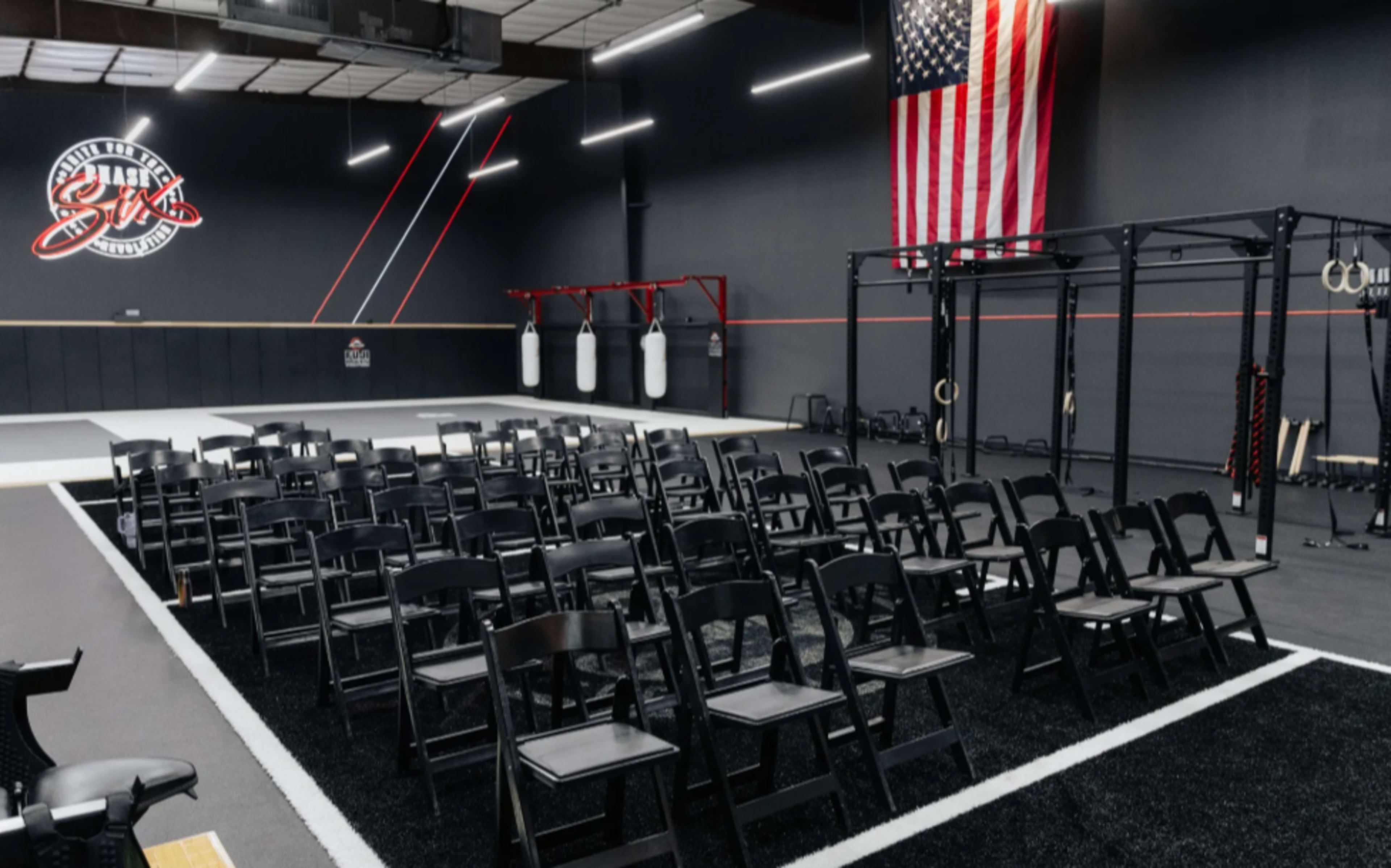 The image shows a gymnasium setup with rows of black chairs facing a training area, featuring boxing bags, workout equipment, and an American flag on the wall.