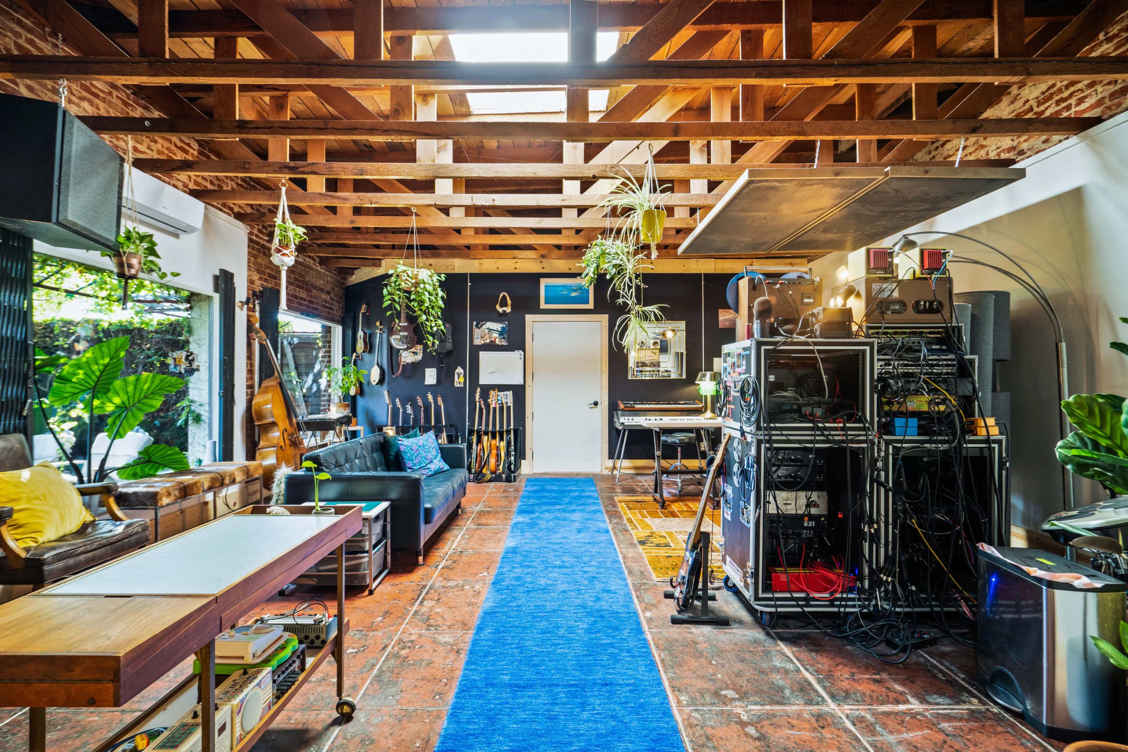 A spacious room with exposed wooden beams, various musical instruments, and a wall of audio equipment, featuring a blue runner rug down the center.