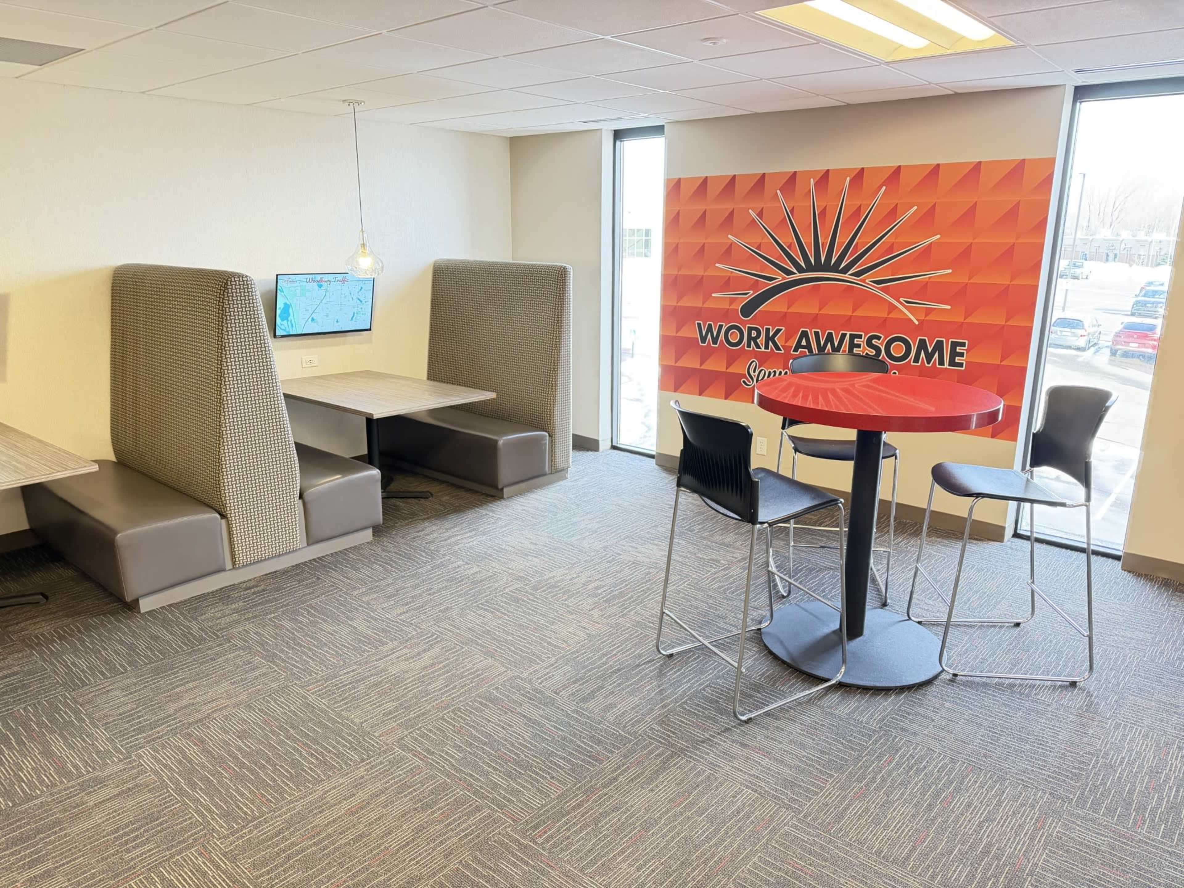The image shows a modern office space with two booth seating areas and a circular table with chairs, alongside a colorful wall that reads "WORK AWESOME."
