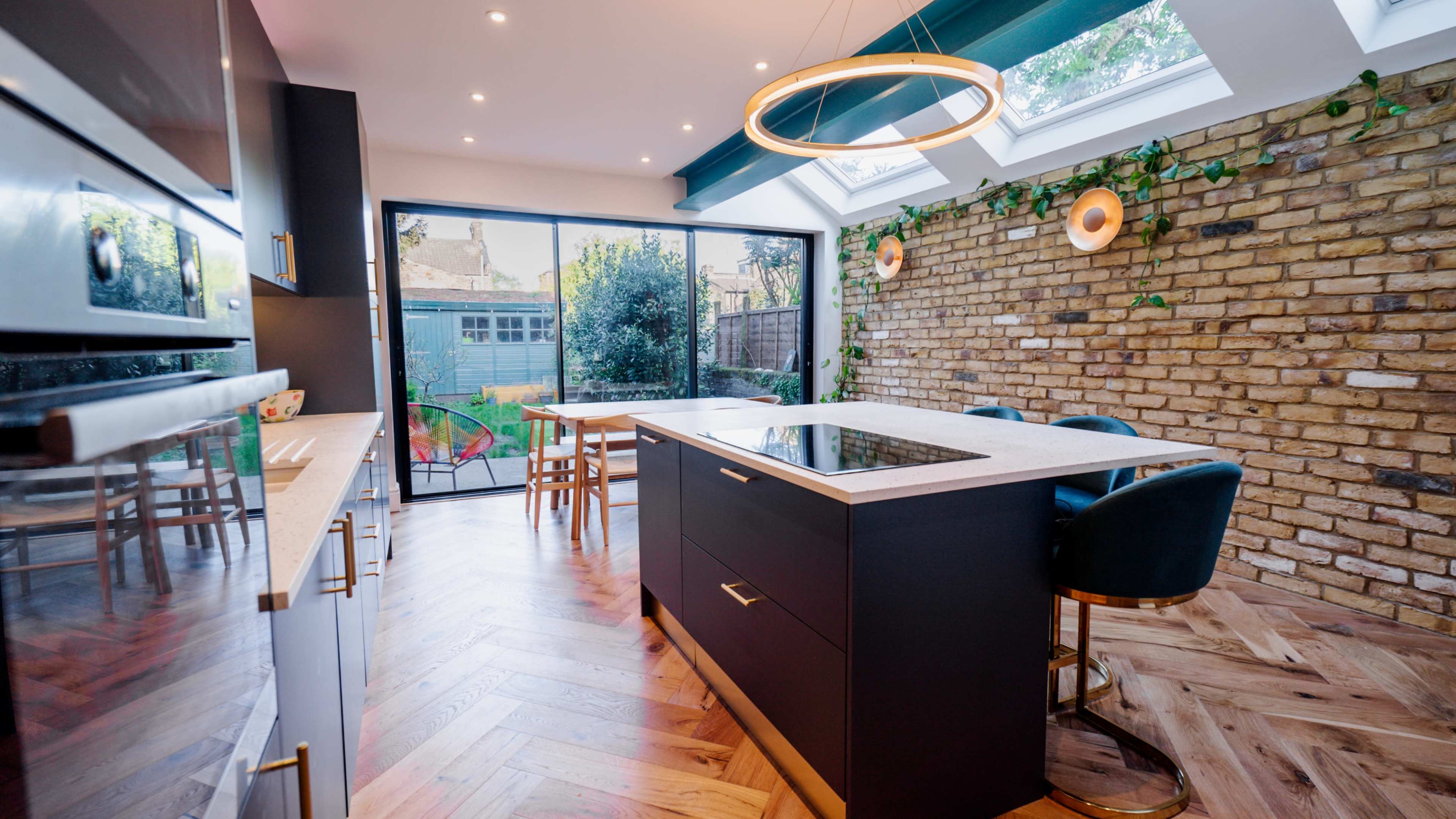 A modern kitchen features a central island with a cooktop, surrounded by wooden flooring and large glass doors leading to a garden.