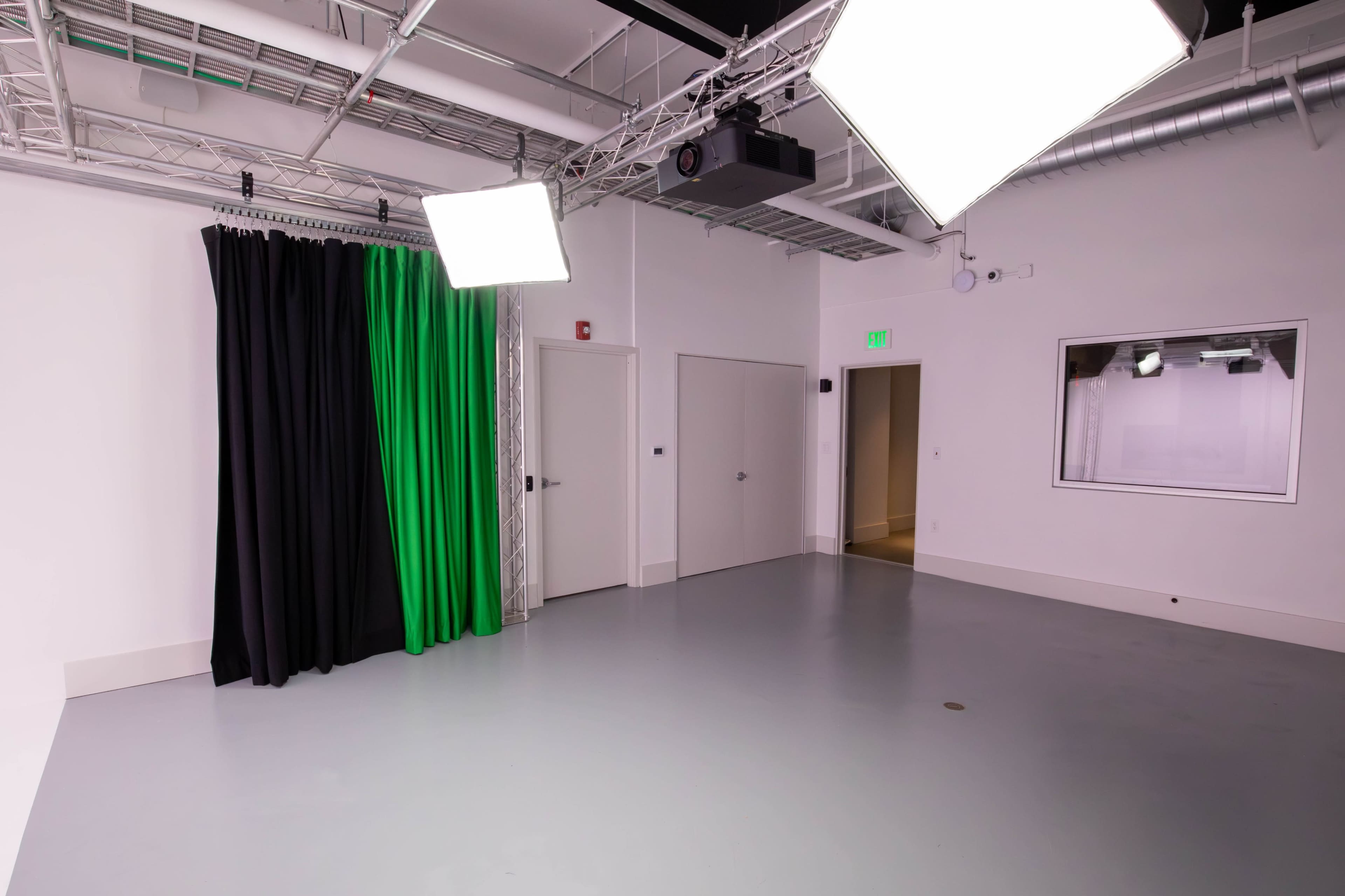 The image shows a studio space featuring green and black curtains, a gray floor, and multiple overhead lights.