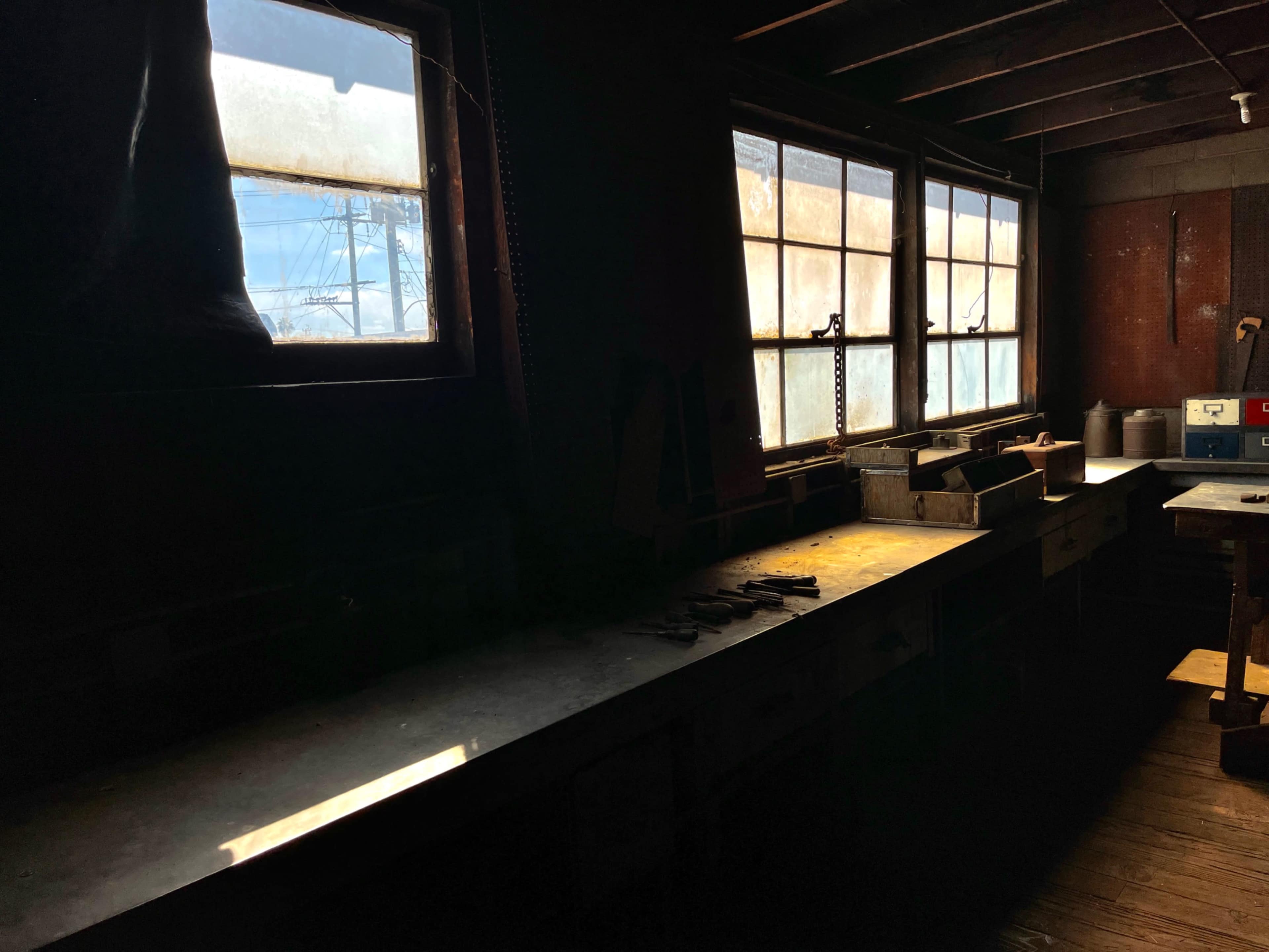 A dimly lit workshop features a long countertop with tools and two windows allowing faint light to enter.