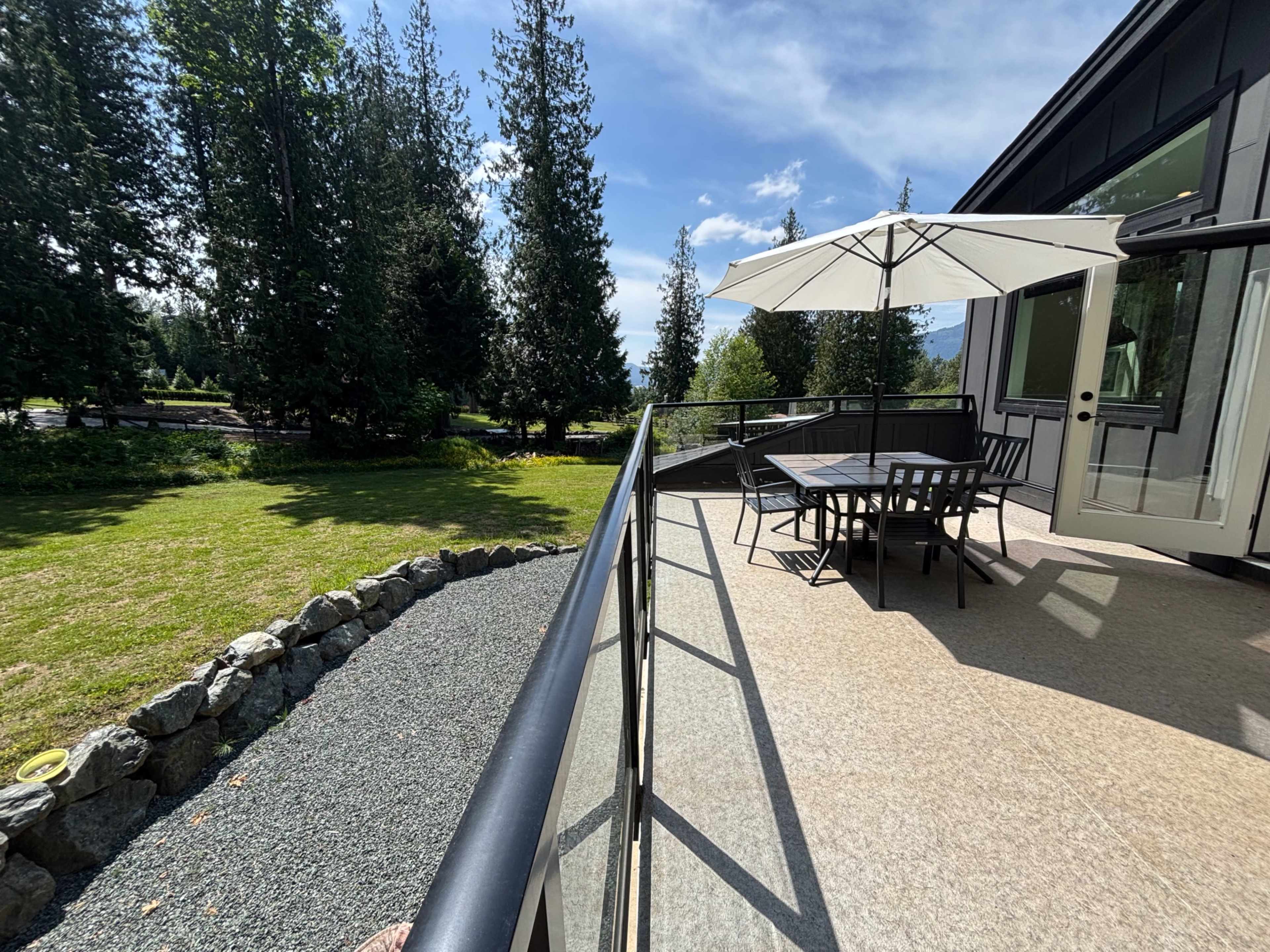 A patio with a table and umbrella overlooks a grassy area and dense trees in the background.