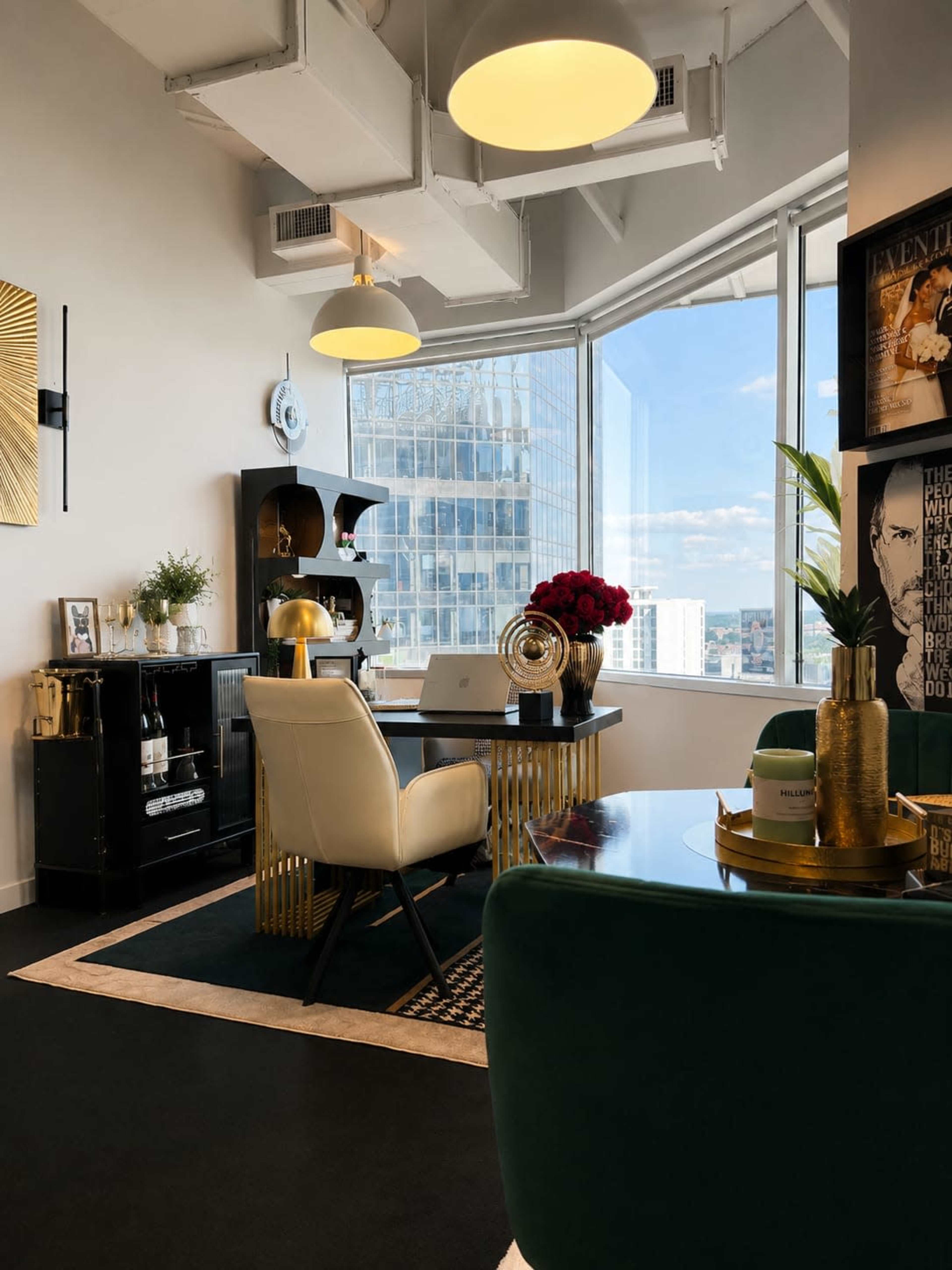 The image shows a modern office space with large windows, stylish furniture, and decorative items like flowers and art pieces.