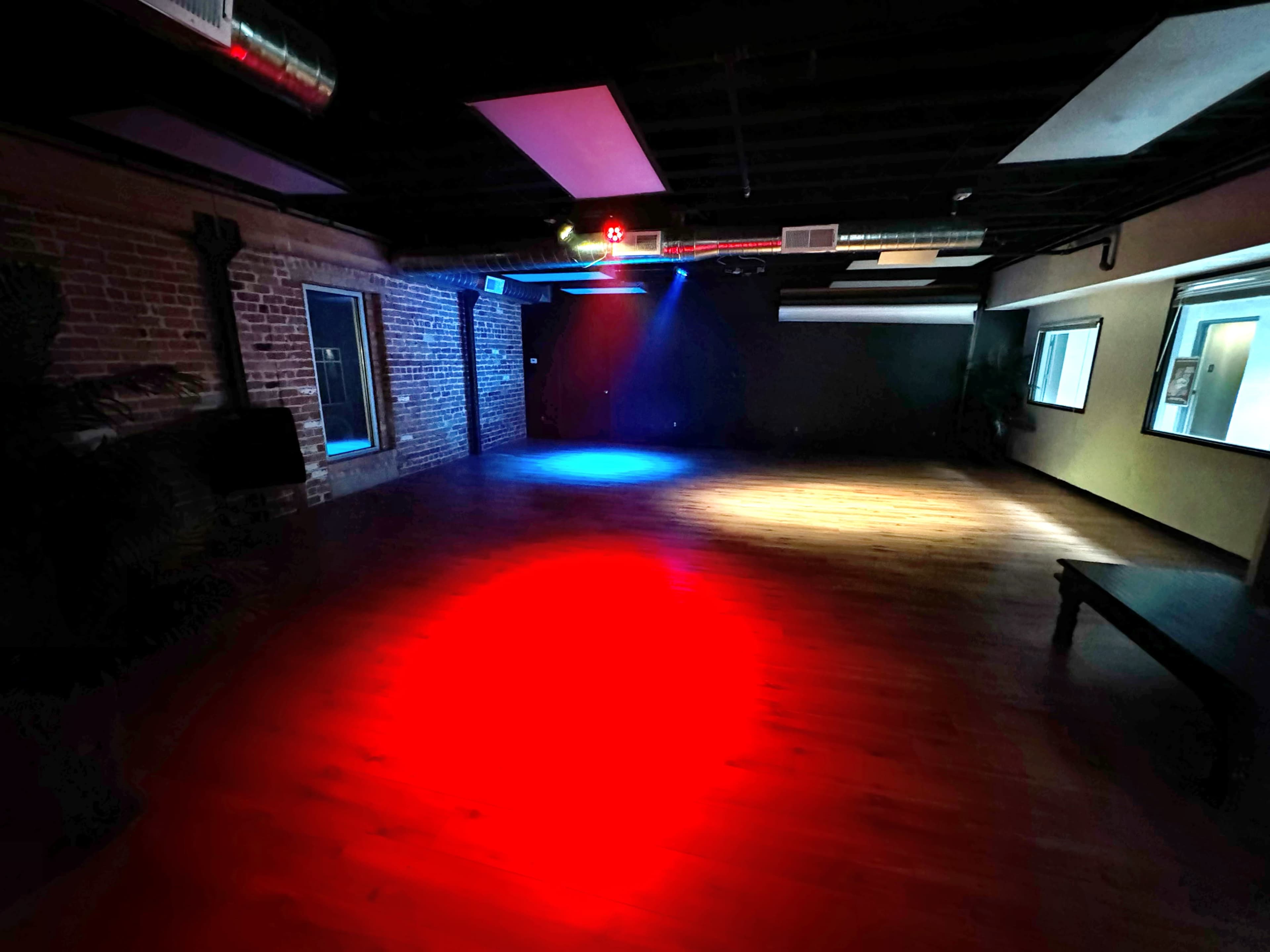 The room features hardwood flooring illuminated by red and blue lights, with exposed brick walls and several windows.