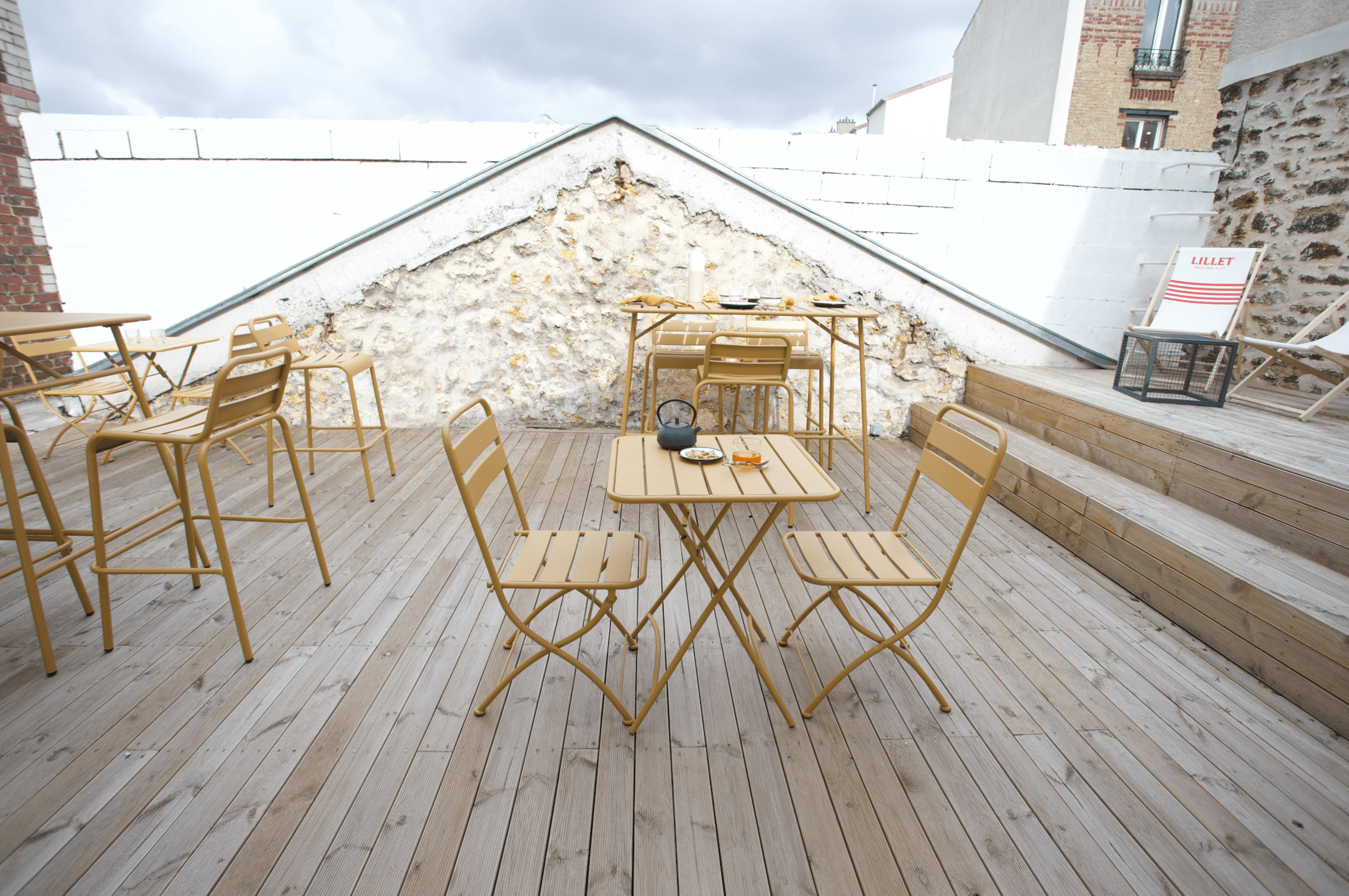 A terrace features yellow metal furniture arranged on wooden decking next to a white wall.