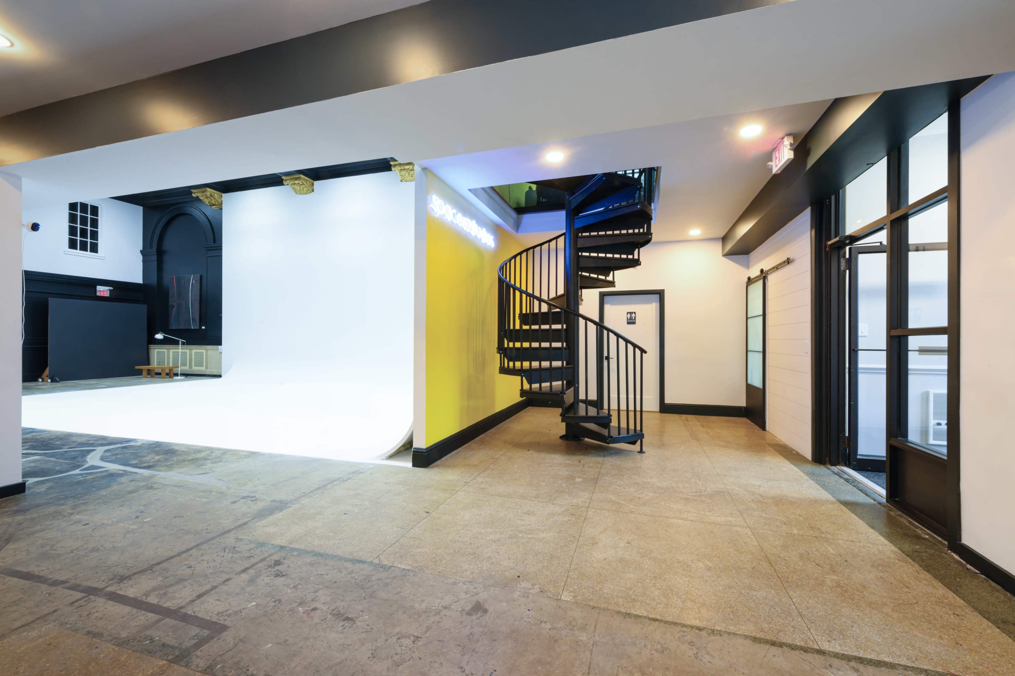 A spacious interior with a spiral staircase leading to an upper level, one wall painted bright yellow, and an open doorway on the right.