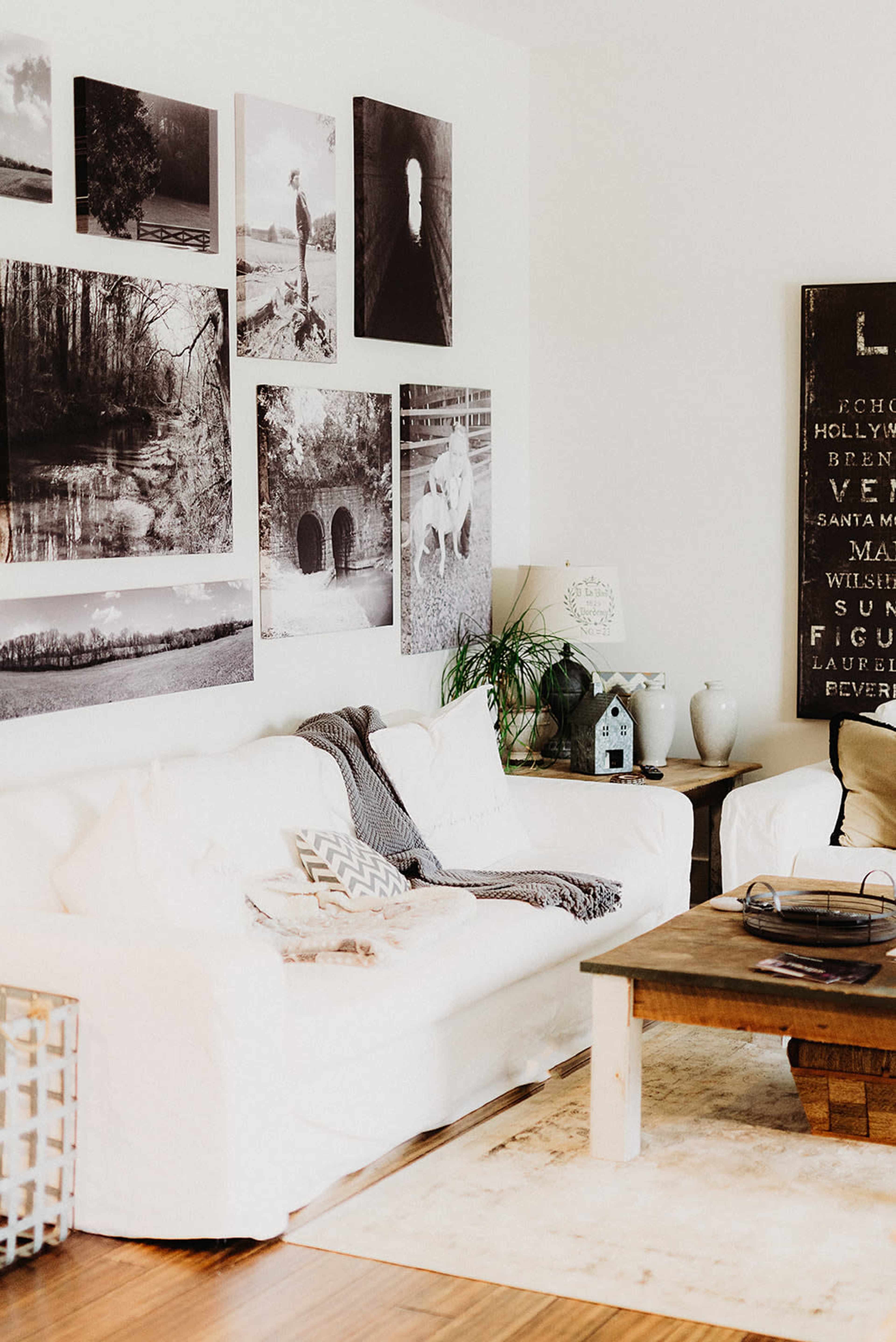 A cozy living room with a white couch, a wooden coffee table, and a wall adorned with black and white photographs.