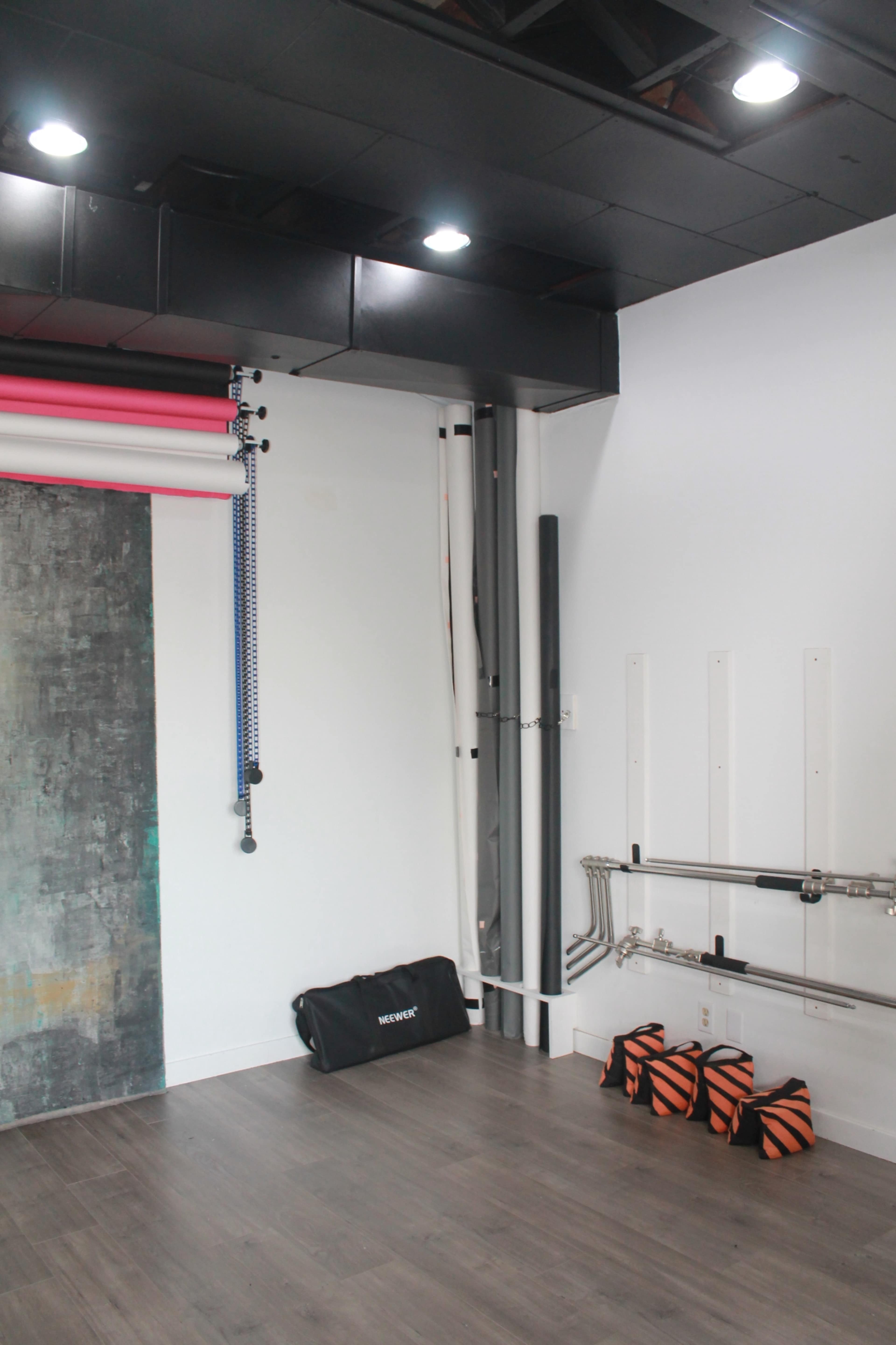 A photography studio with backdrop rolls, a gym bag, and visible plumbing along the walls.