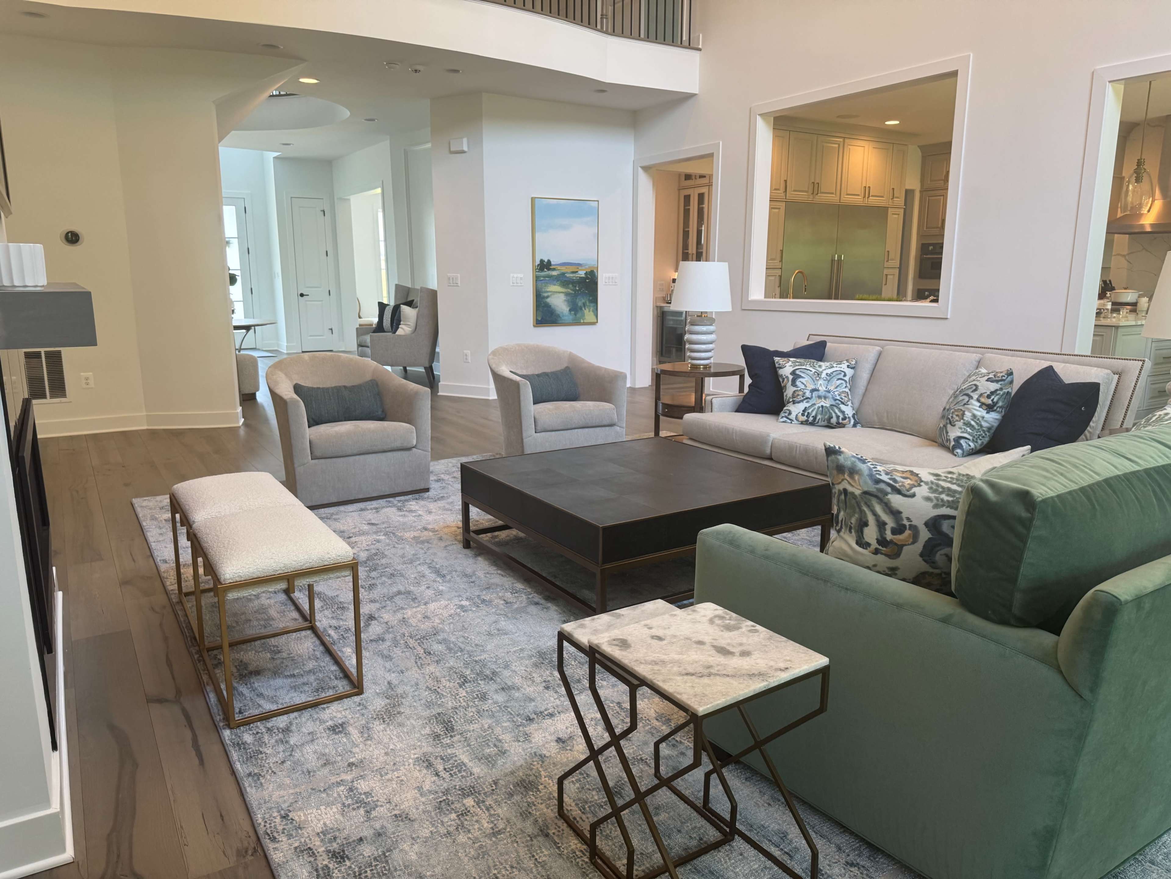 The living room features a light gray sofa, two armchairs, a large coffee table, and a rug, all arranged around a fireplace in a bright, open space.