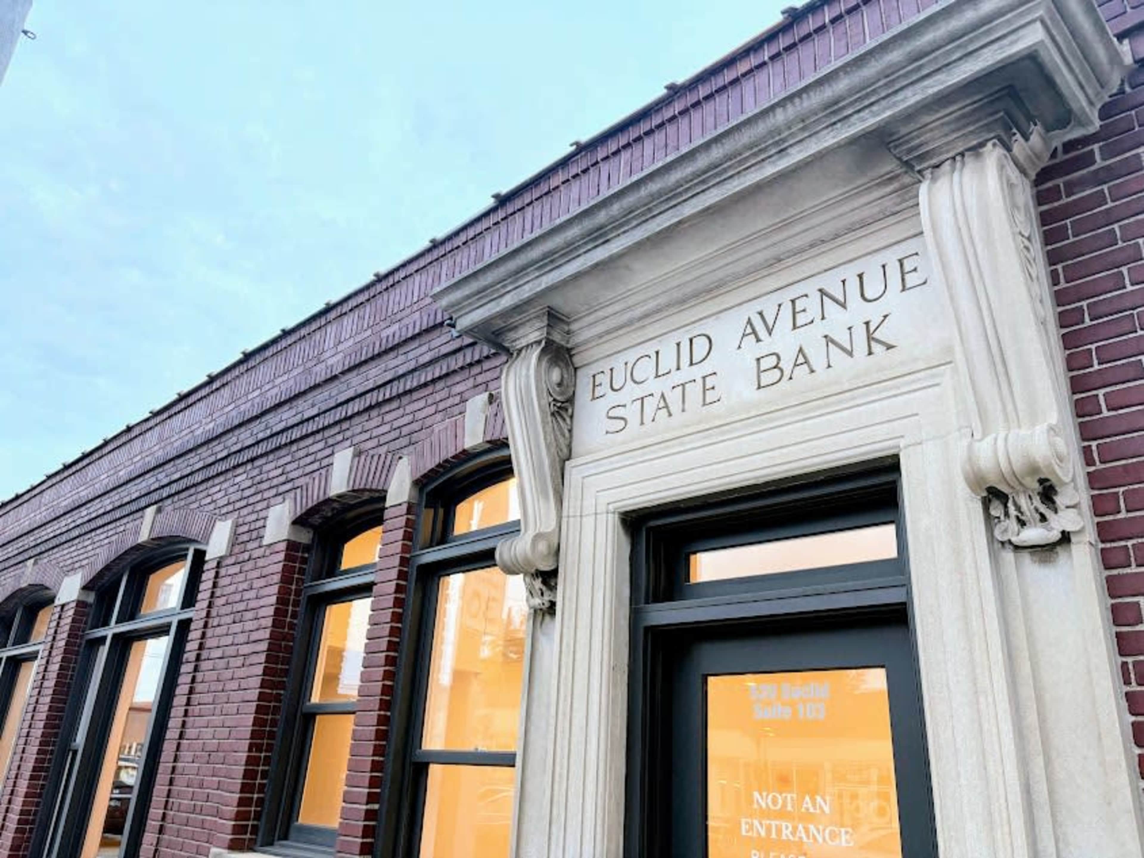 The image shows the exterior of a historical brick building with the words "Euclid Avenue State Bank" carved into a stone arch above a window.