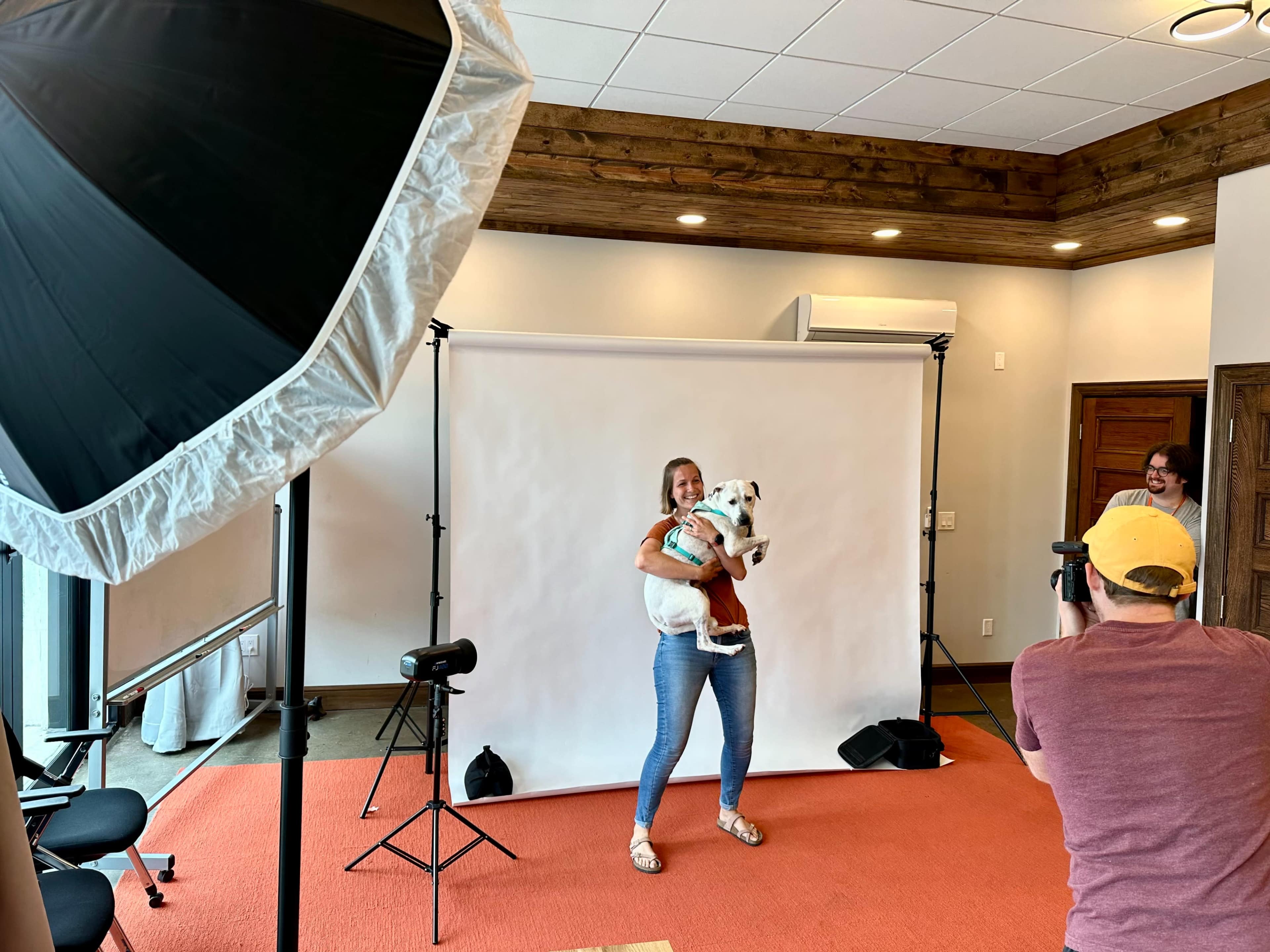 A woman holds a dog in front of a photography backdrop while a photographer captures the moment.