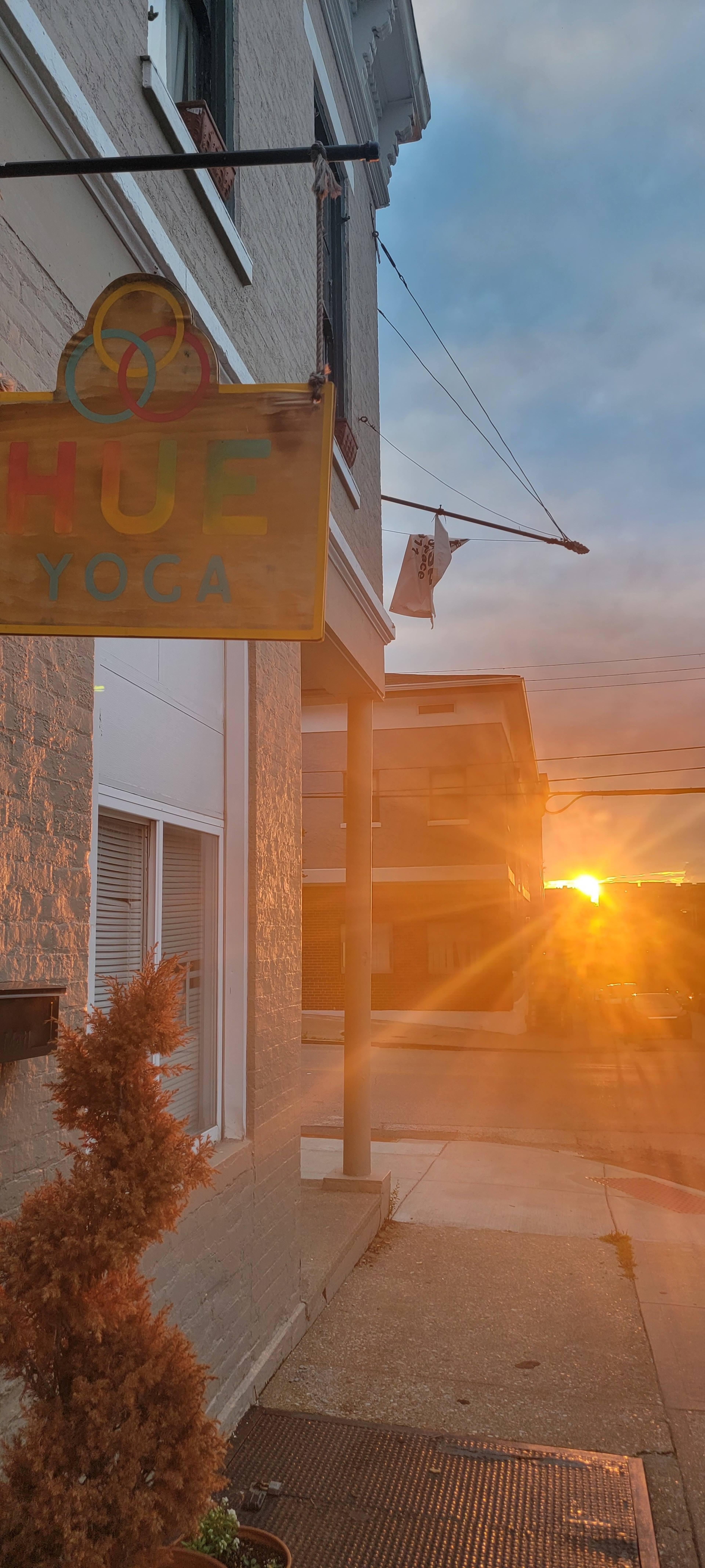 The sun sets behind a building near a yoga studio sign that reads "HUF YOGA."