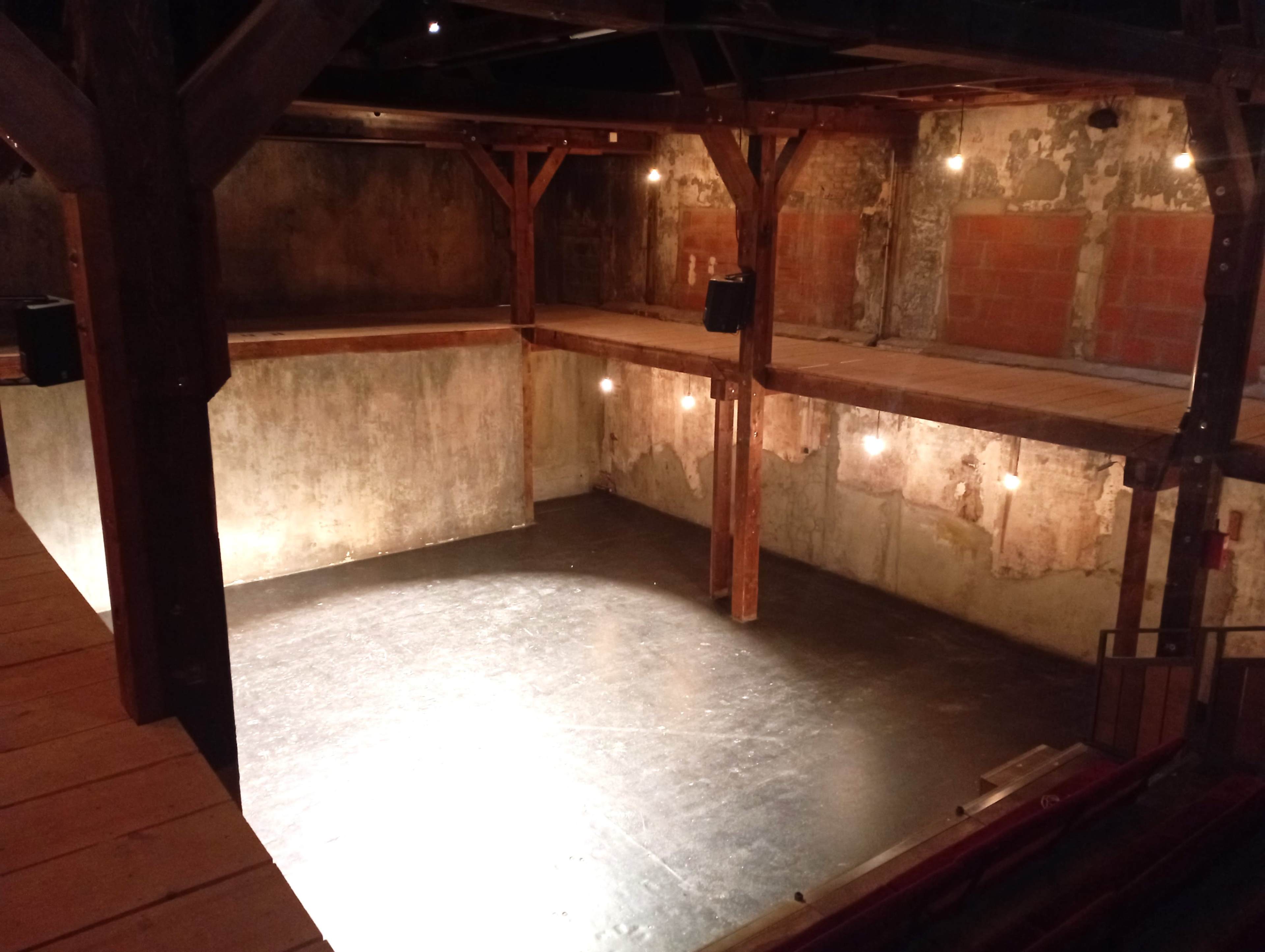 A circular, multi-level performance space with rustic wooden beams and a dimly lit floor.