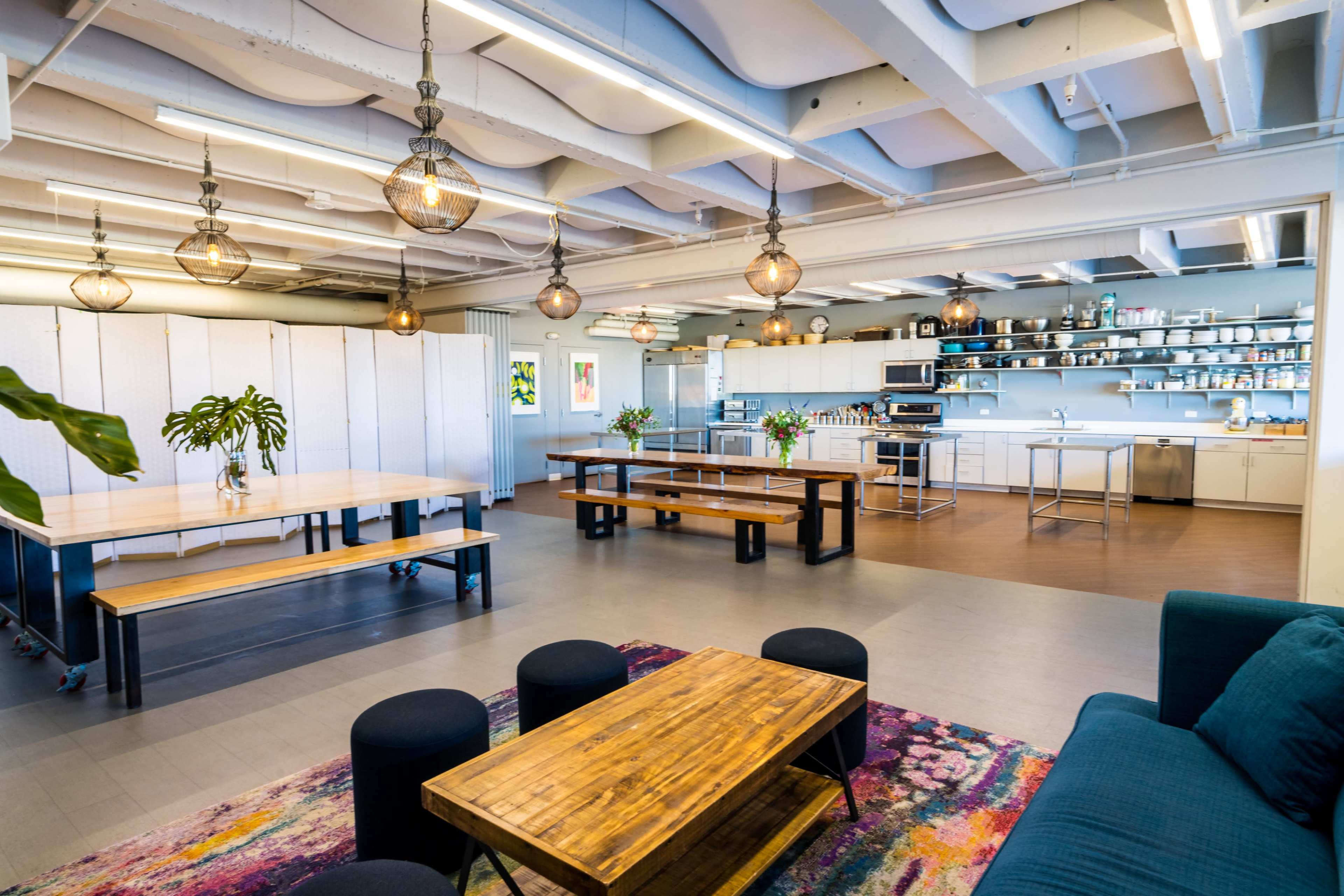A modern kitchen and dining area with wooden tables, dark seating, and a well-organized kitchen space featuring shelves and appliances.