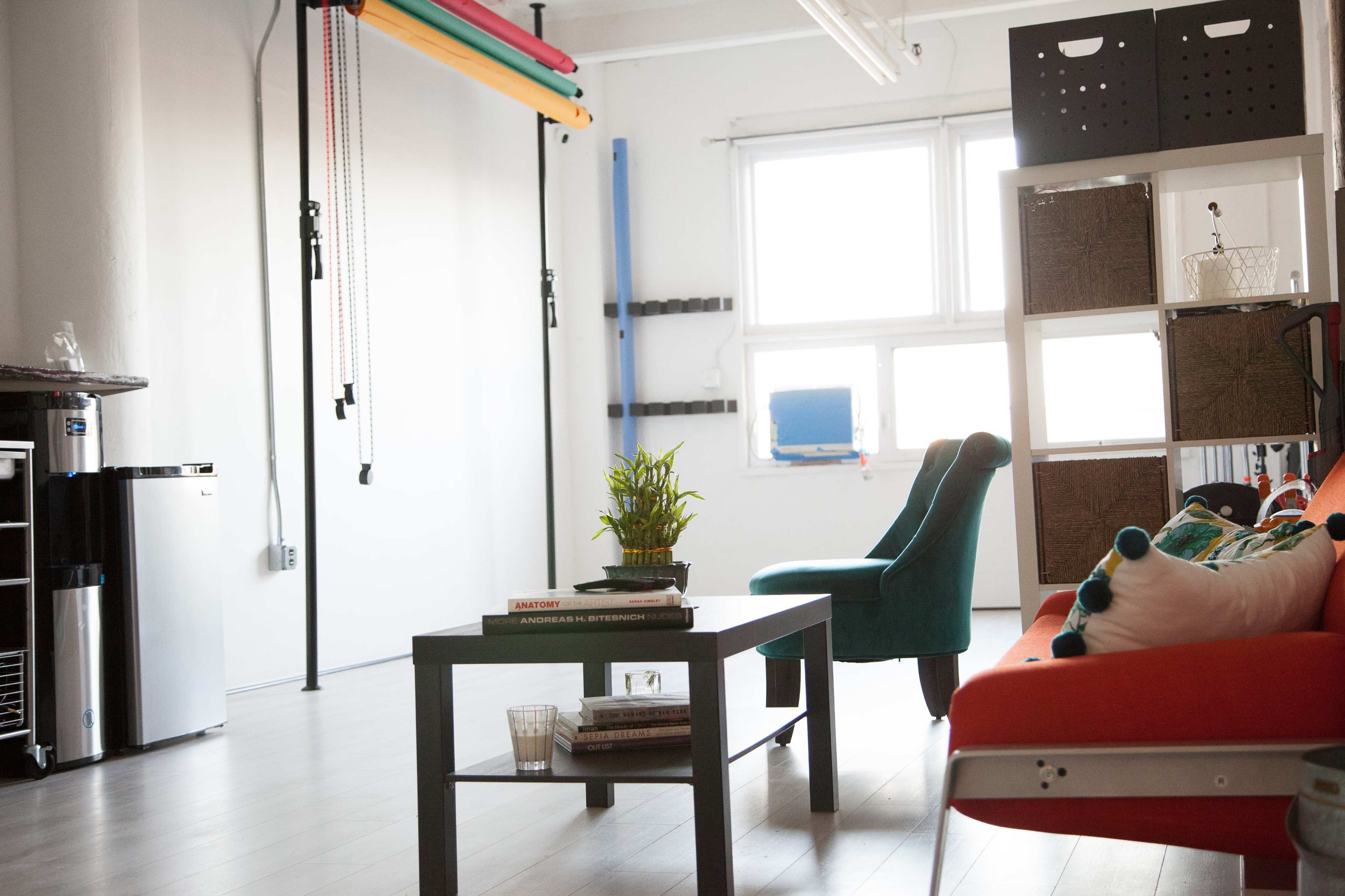 A bright room features a red sofa, a green chair, a coffee table, and various storage bins along the walls.