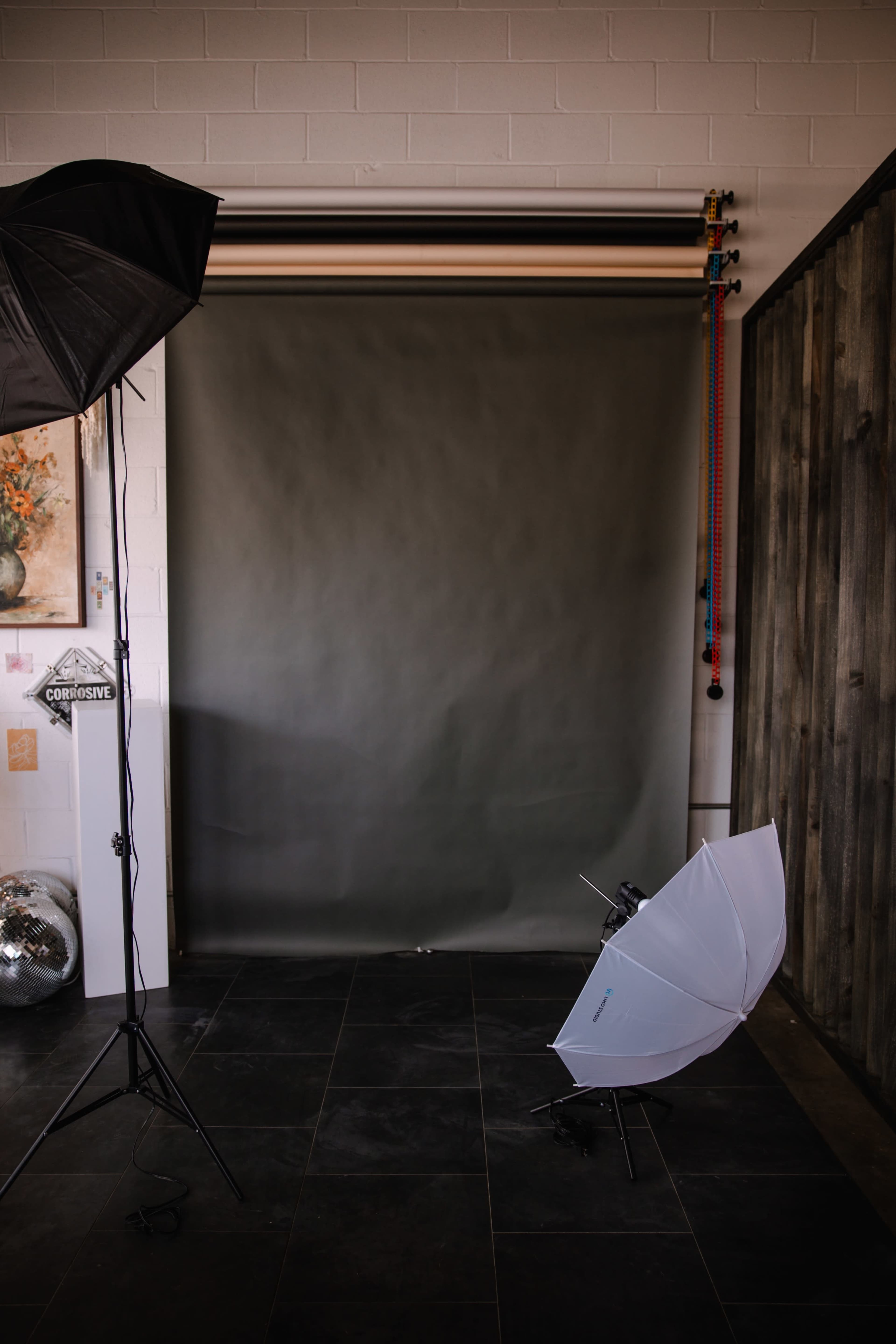 A photography studio setup featuring a gray backdrop, light stands, and softboxes positioned on a tiled floor.