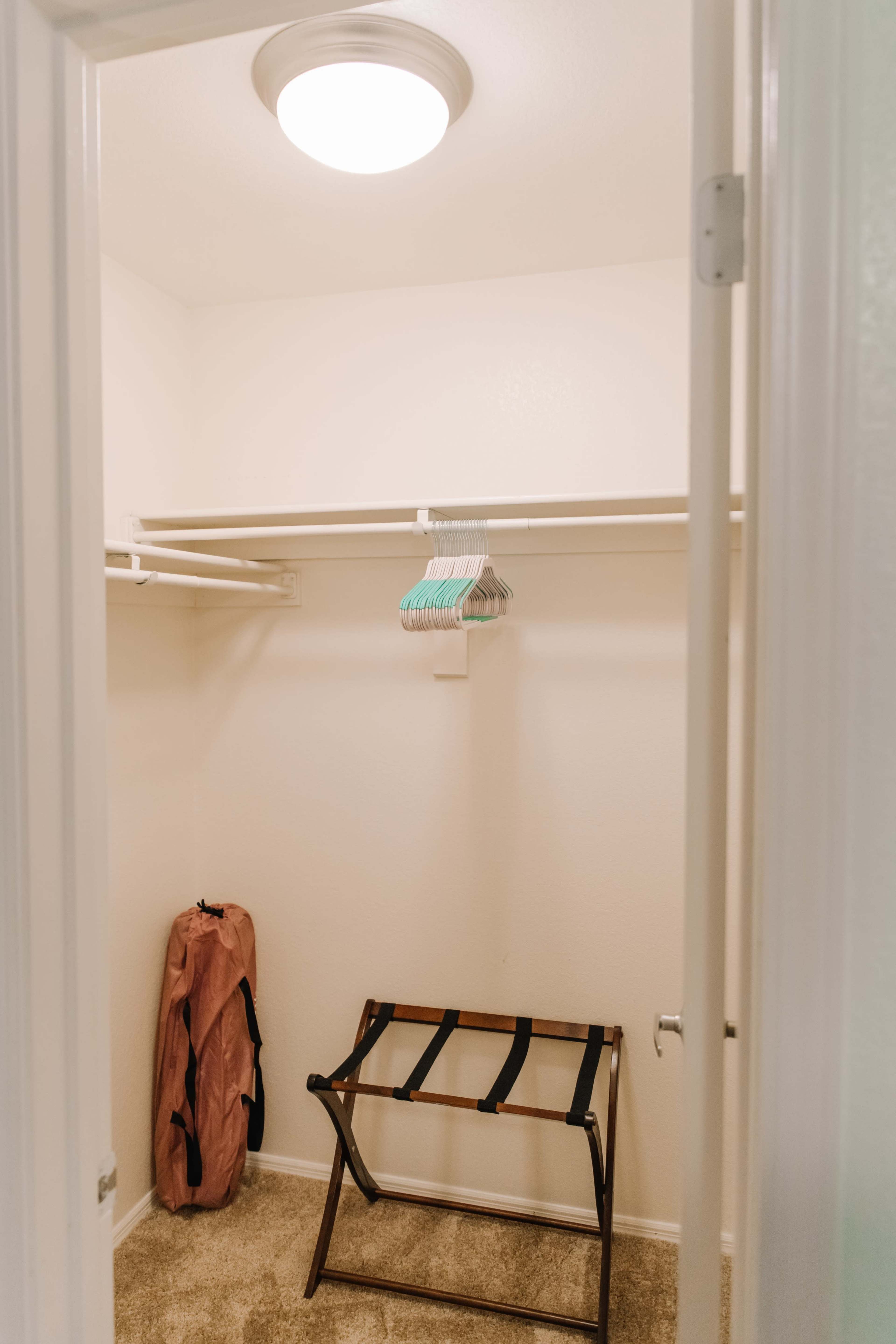 A small walk-in closet with a clothes rack, a folding clothes hanger stand, and a pink garment bag against the wall.