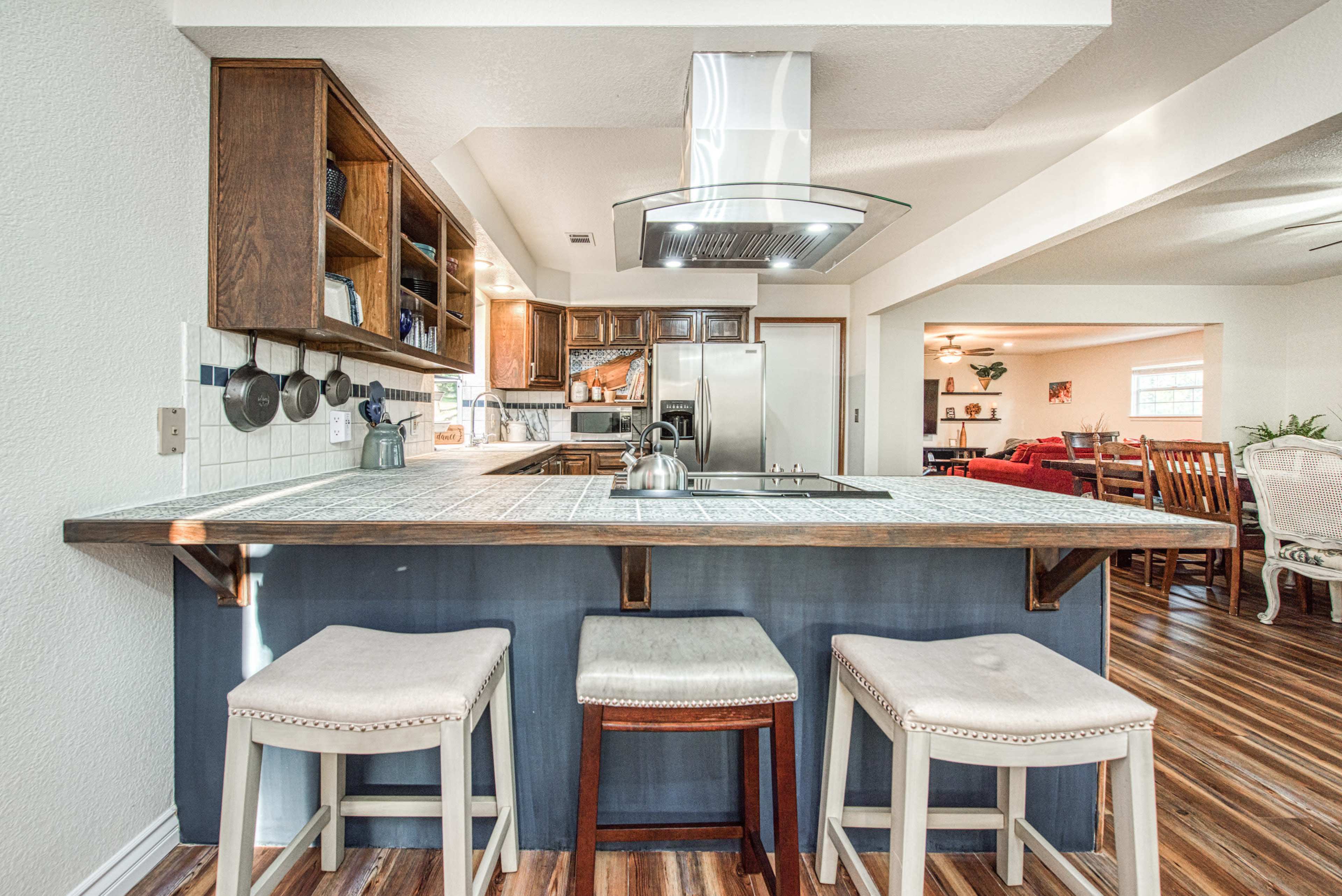 A modern kitchen with a center island, featuring three bar stools and stainless steel appliances in the background.